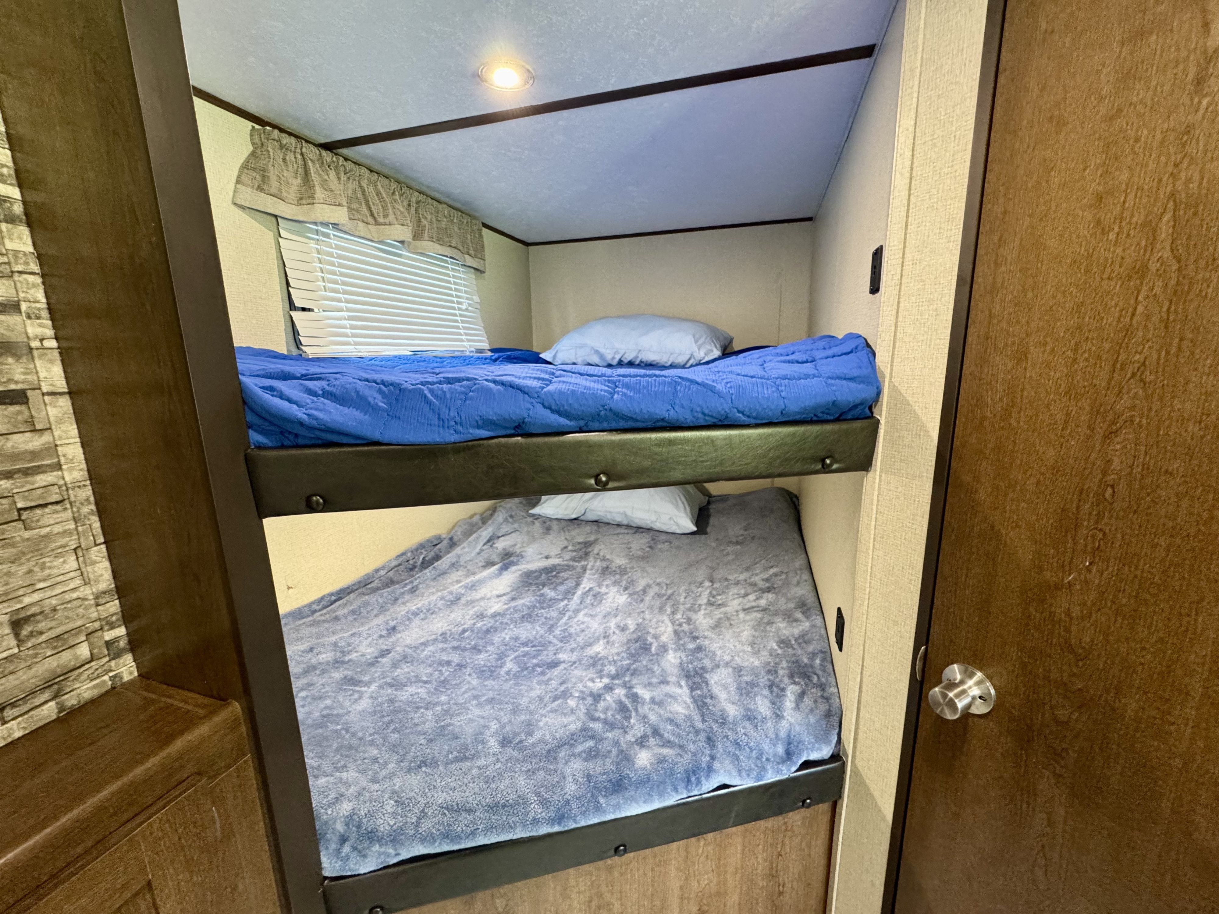 Cozy bunk beds in this rv rental, featuring soft blue bedding, window blinds, and overhead lighting for comfort.. Avenger ATI 2020