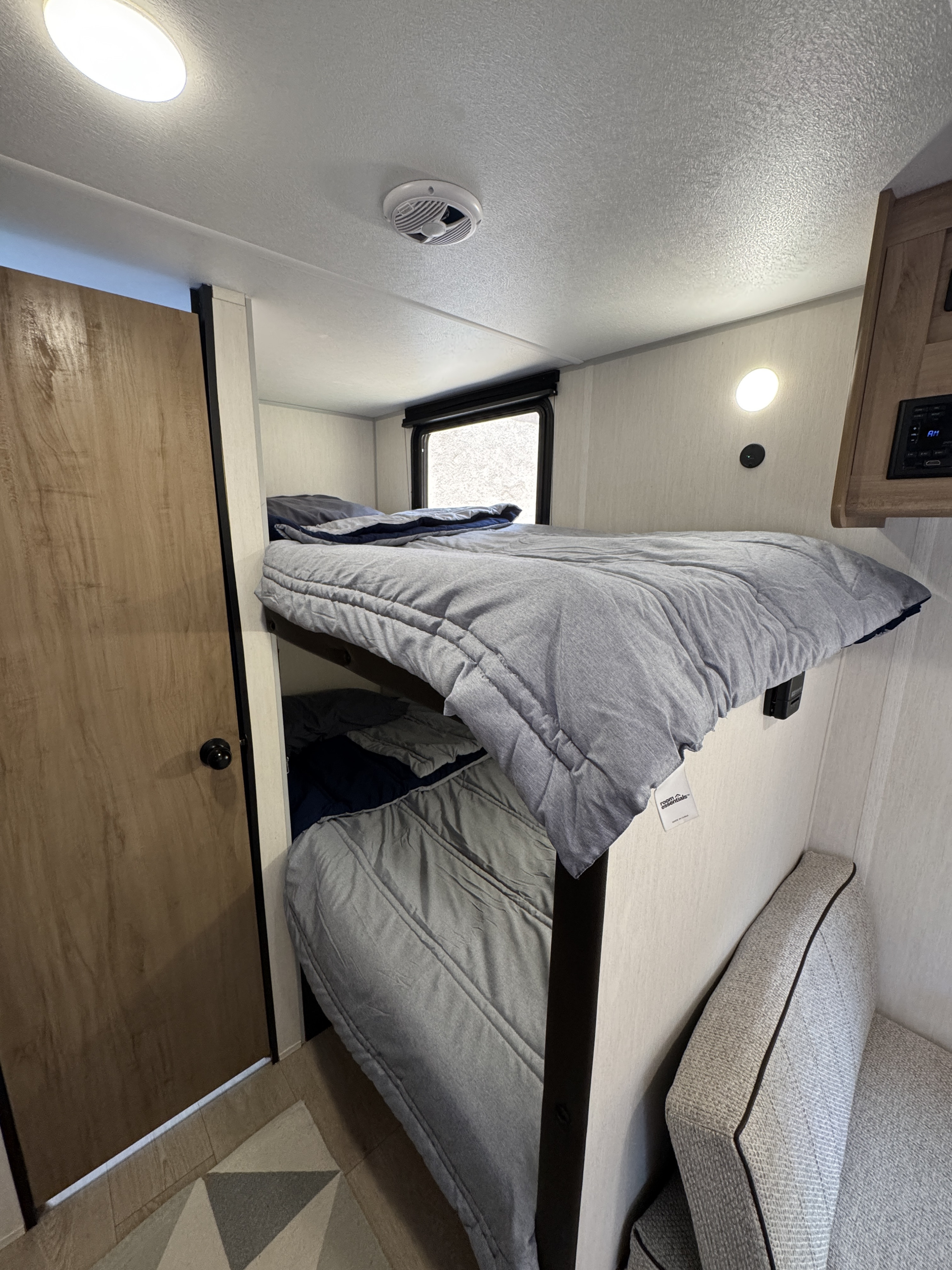 Inside an RV rental: comfy bunk beds with gray bedding, a window, and a door. Perfect for a family trip.. Forest River Cherokee Wolf Pup 2025