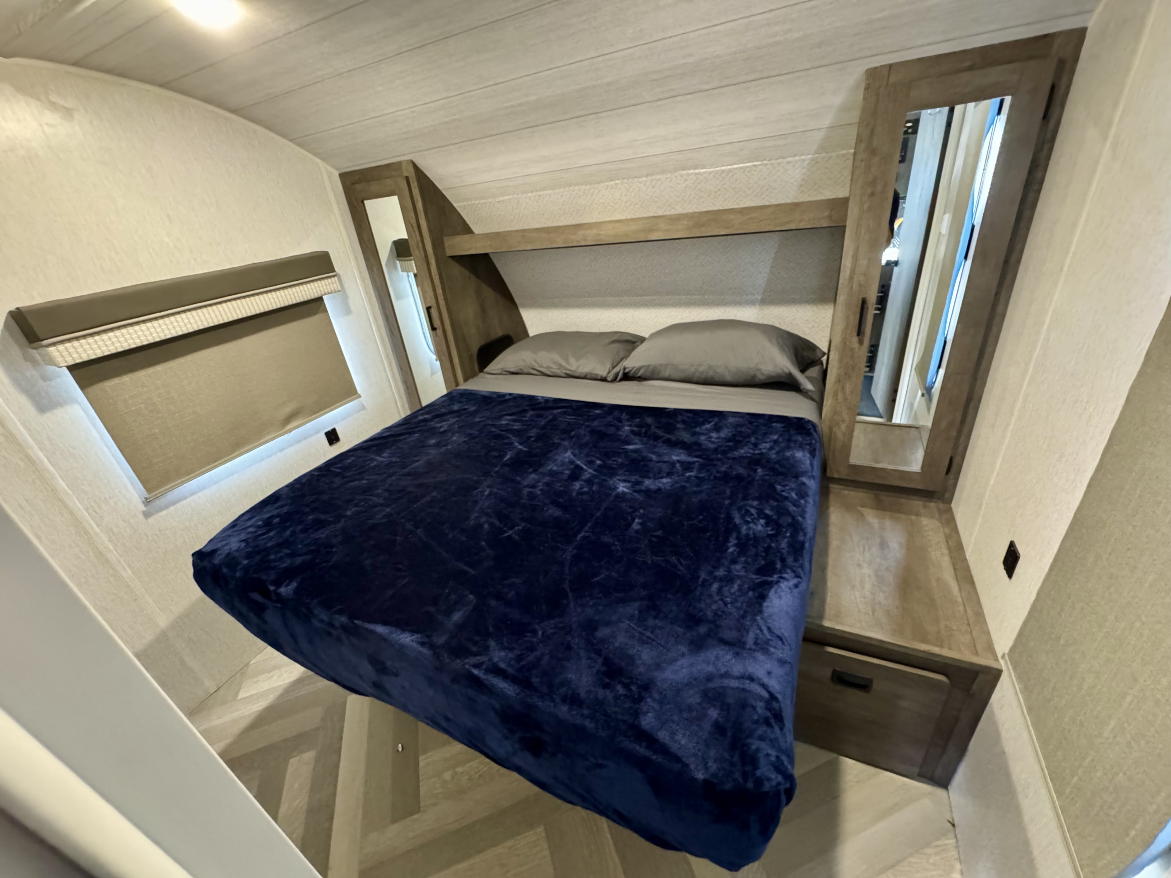 Cozy RV rental bedroom with a bed, pillows, blue blanket, window shade, and mirrored cabinet. Perfect for travel.. Forest River Salem Cruise Lite 2022
