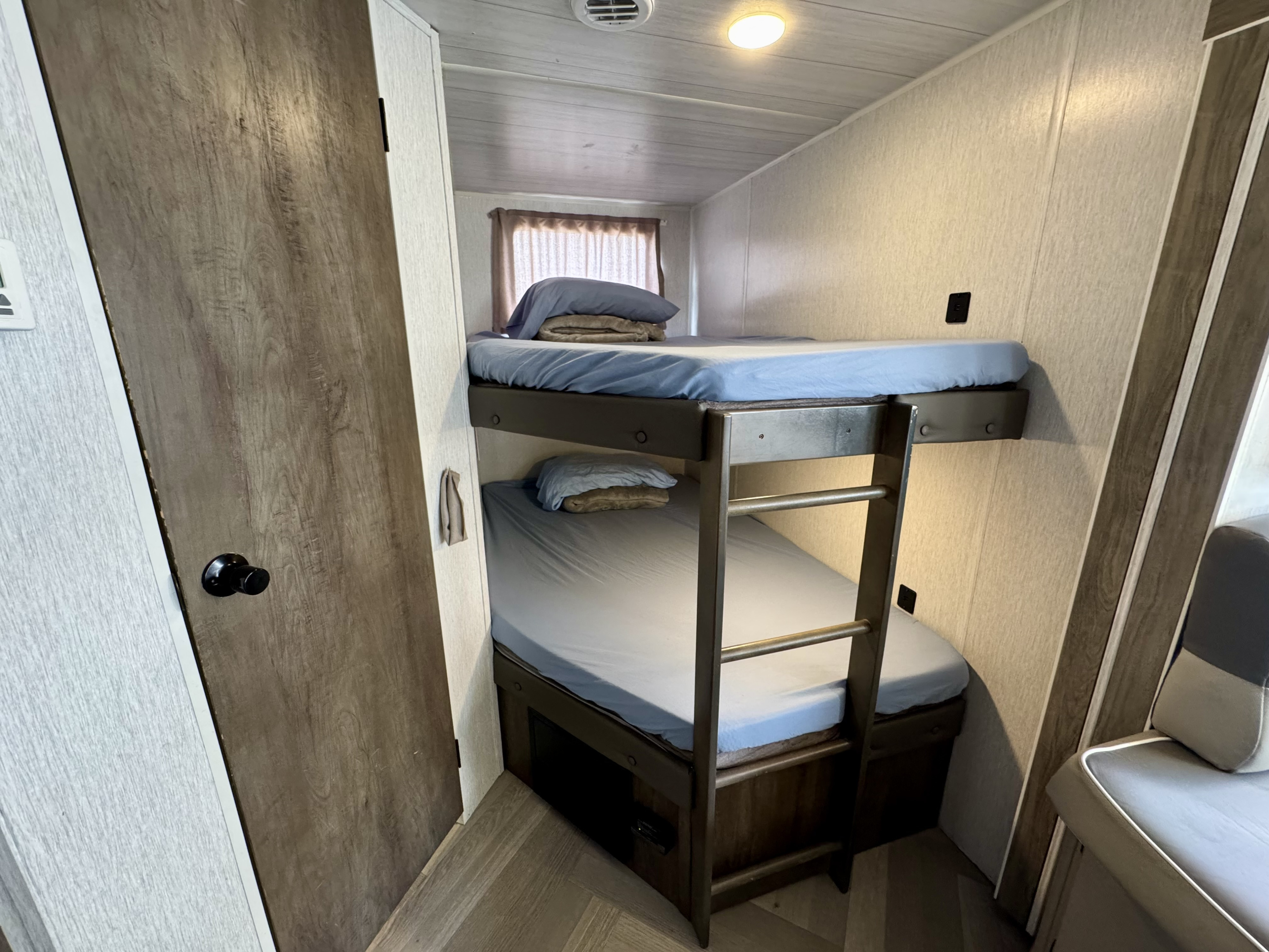 Inside an rv rental, a cozy bunk bed area with blue sheets, a sturdy ladder, and wood-look flooring. Perfect for travelers.. Forest River Salem Cruise Lite 2022