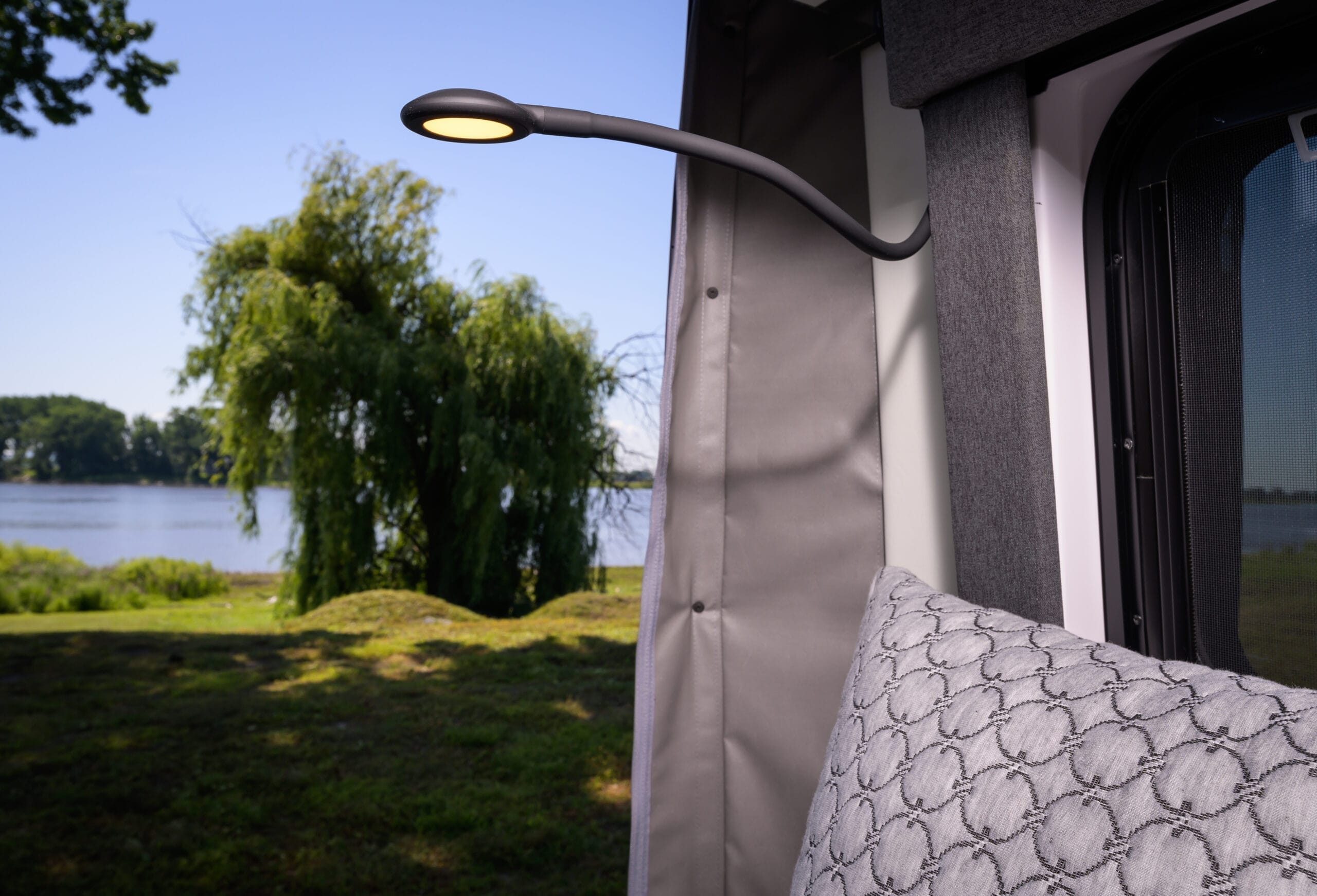 Cozy RV rental interior with a reading light & a tranquil lake view. Ideal for your next campervan adventure.. Other Gala Montecarlo 2025
