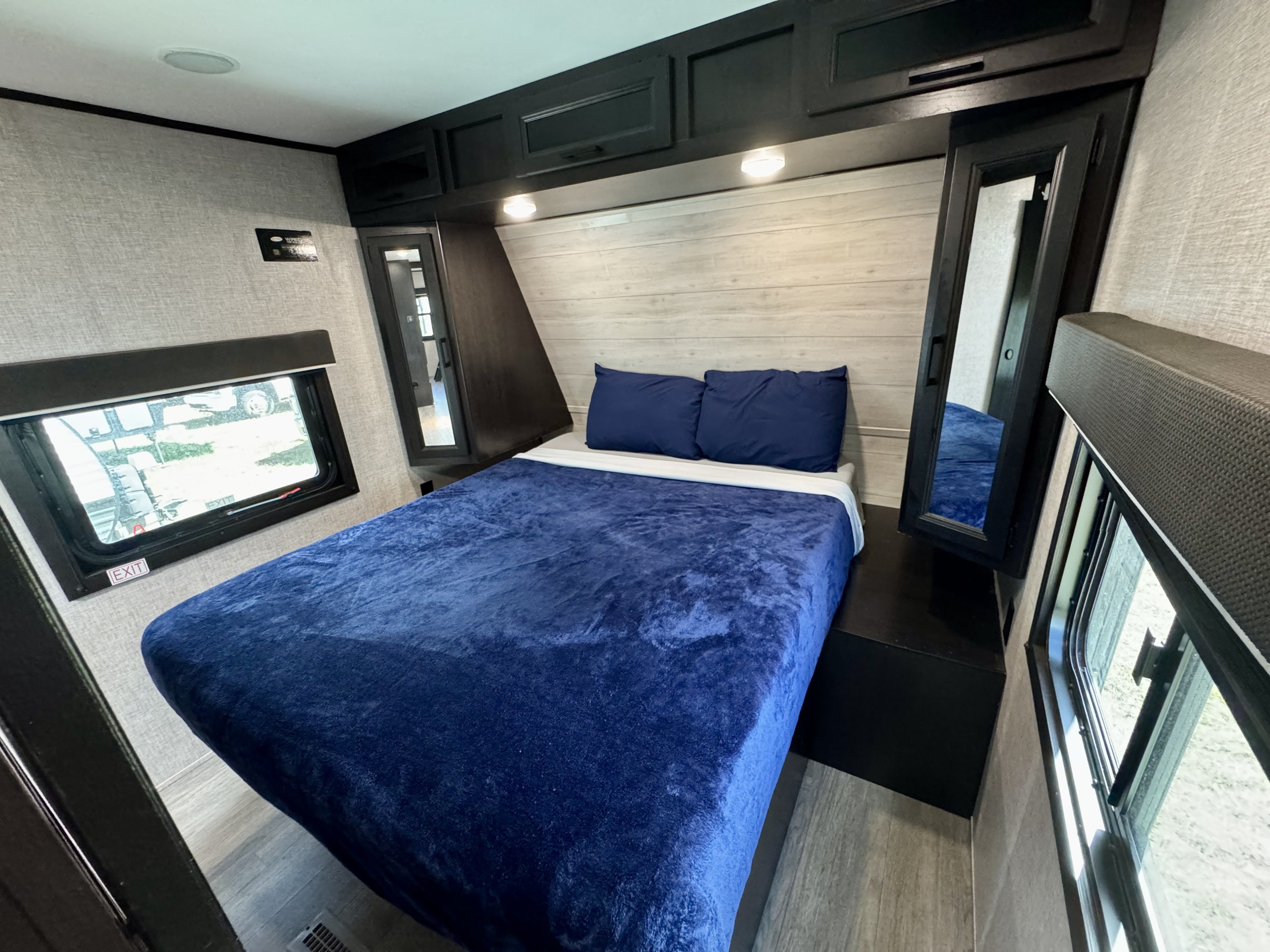 This cozy RV rental bedroom features a comfy bed with blue bedding, overhead storage, two windows, and light flooring.. Jayco Jay Flight 2022