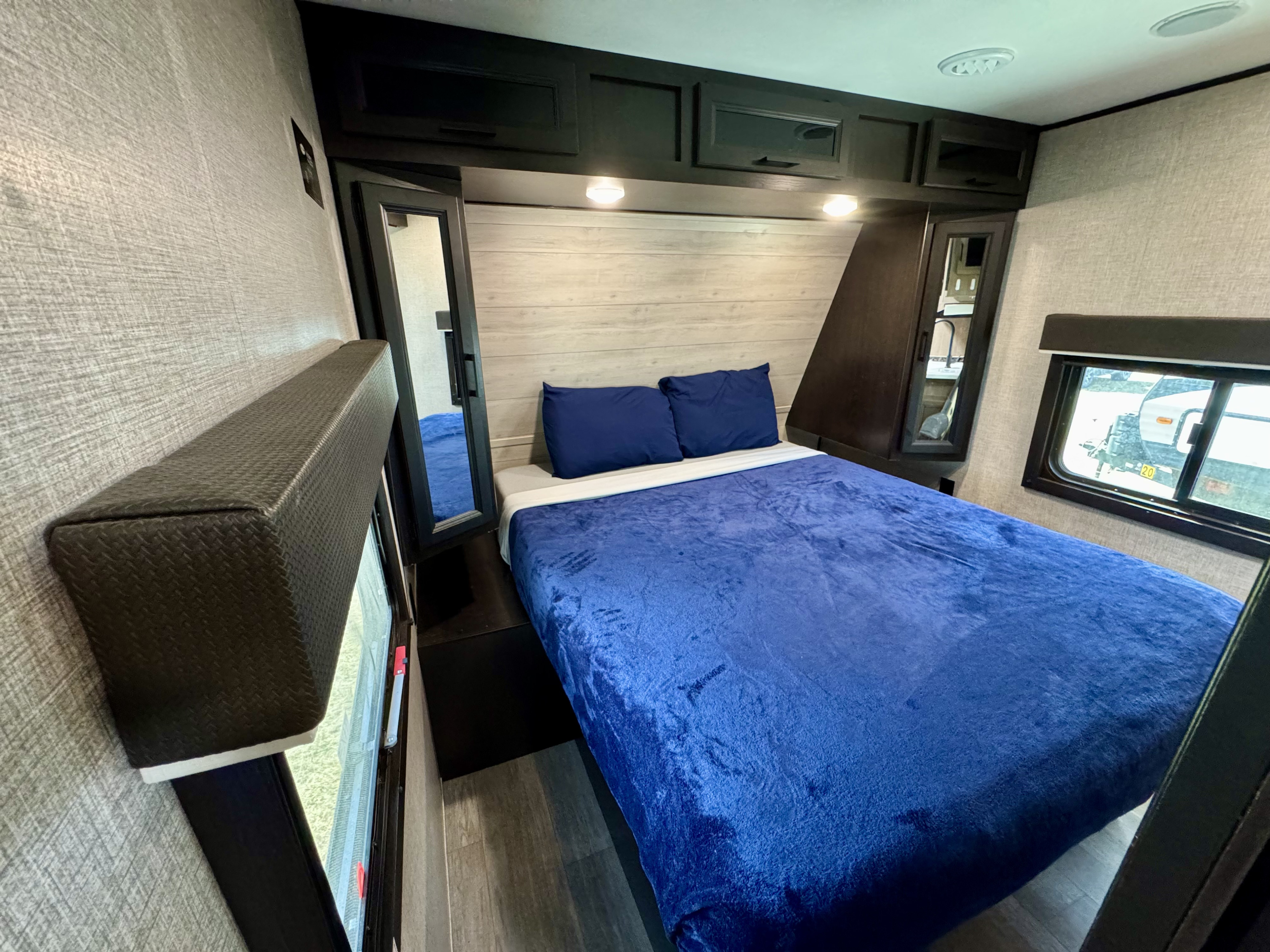 Cozy RV rental bedroom with a blue bed, overhead cabinets, reading lights, and a window. Perfect for comfortable mobile living.. Jayco Jay Flight 2022