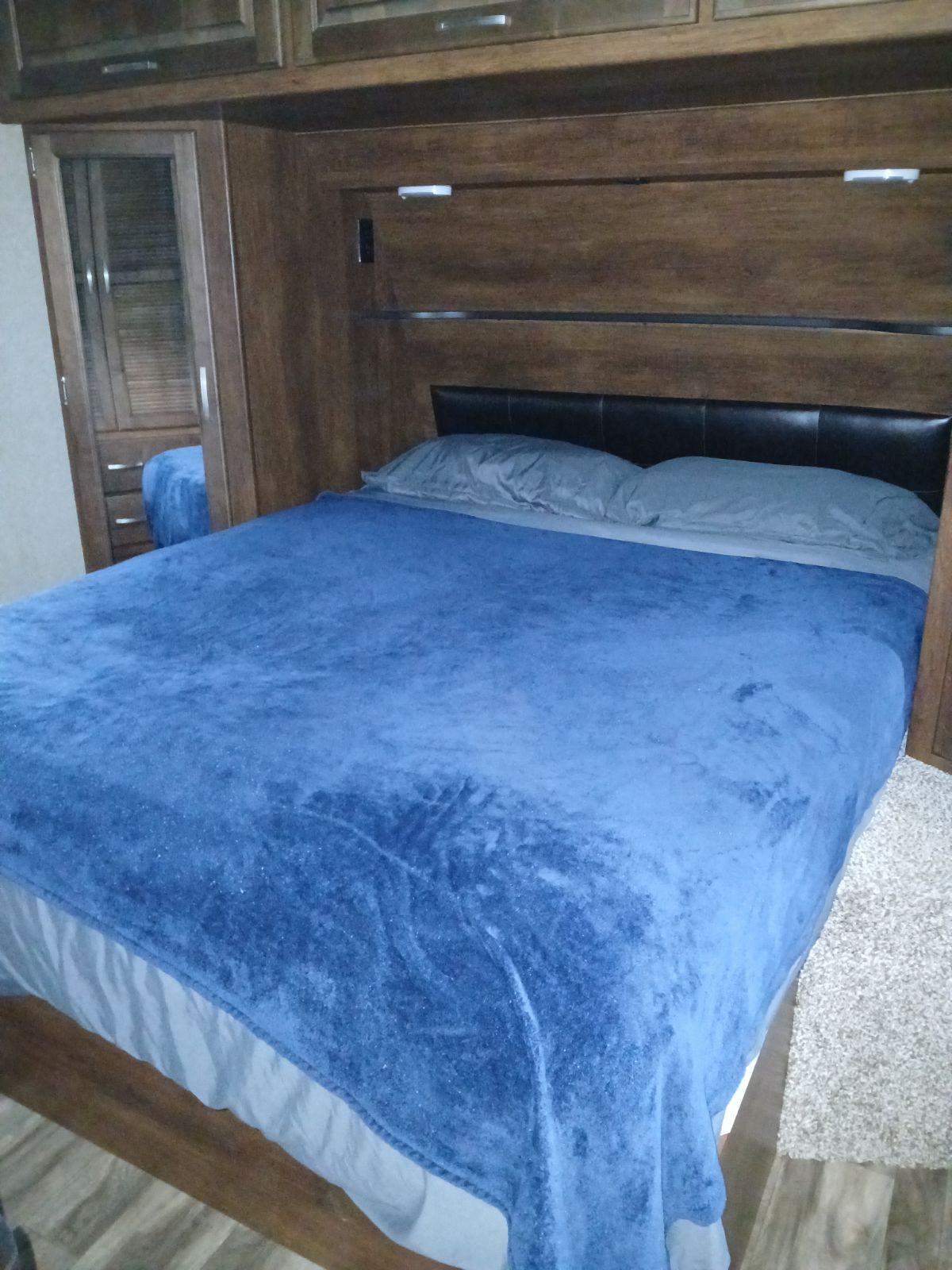 Comfortable RV rental bedroom featuring a bed with a blue blanket, mirrored closet, and built-in wooden cabinetry.. Grand Design Reflection 2019