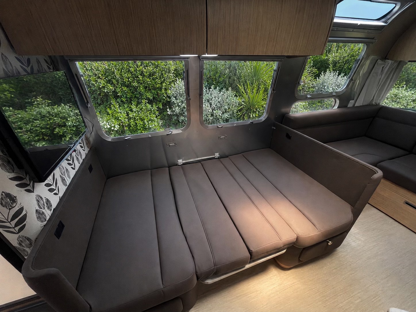 Comfortable RV rental interior features a convertible bed/sofa, panoramic windows with lush nature views, and a TV for relaxation.. Airstream Flying Cloud 2019
