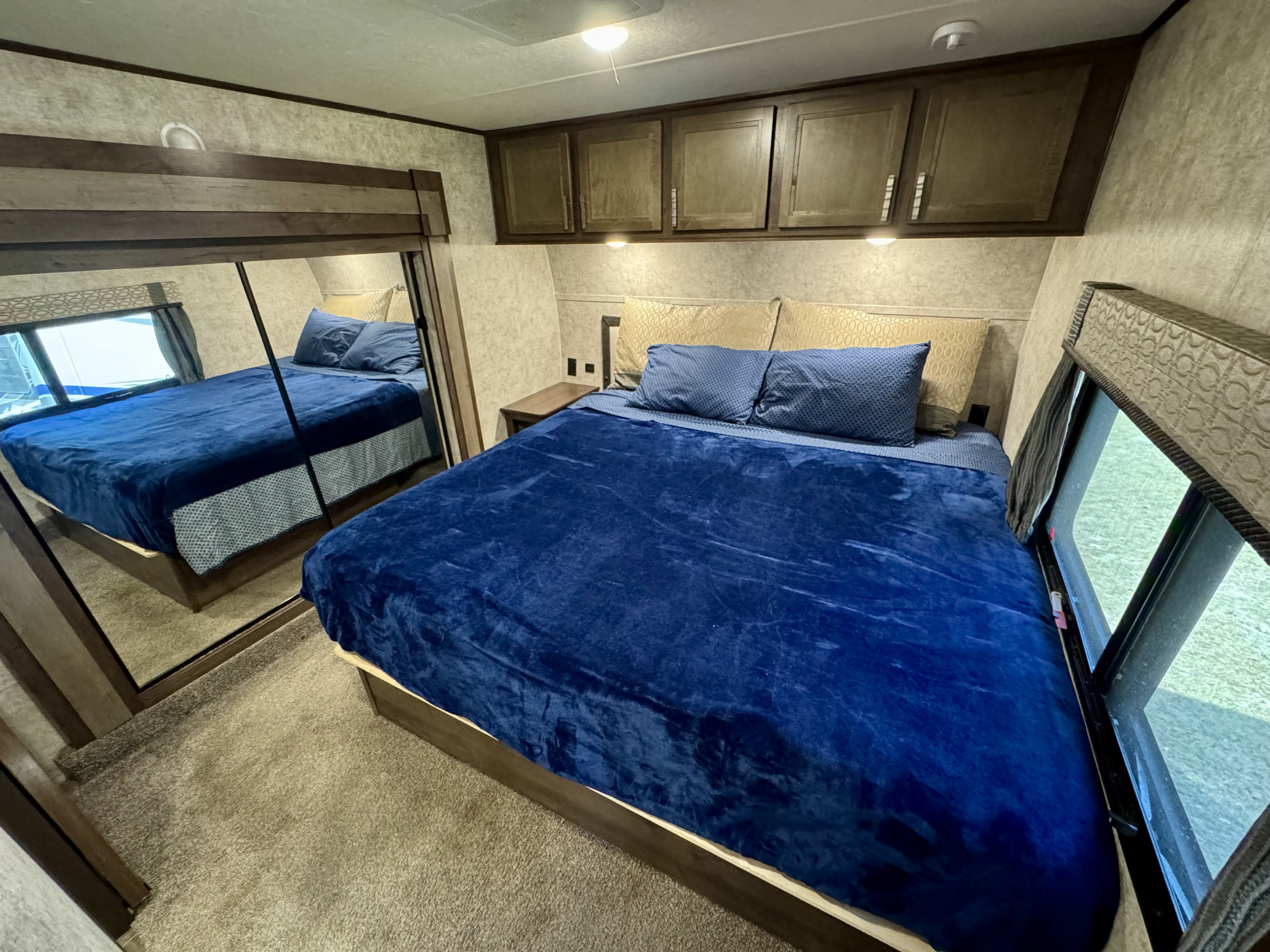 Cozy RV rental bedroom with a large bed, blue bedding, overhead cabinets, and a mirrored closet for comfortable travel.. Highland Ridge RV Mesa Ridge 2018