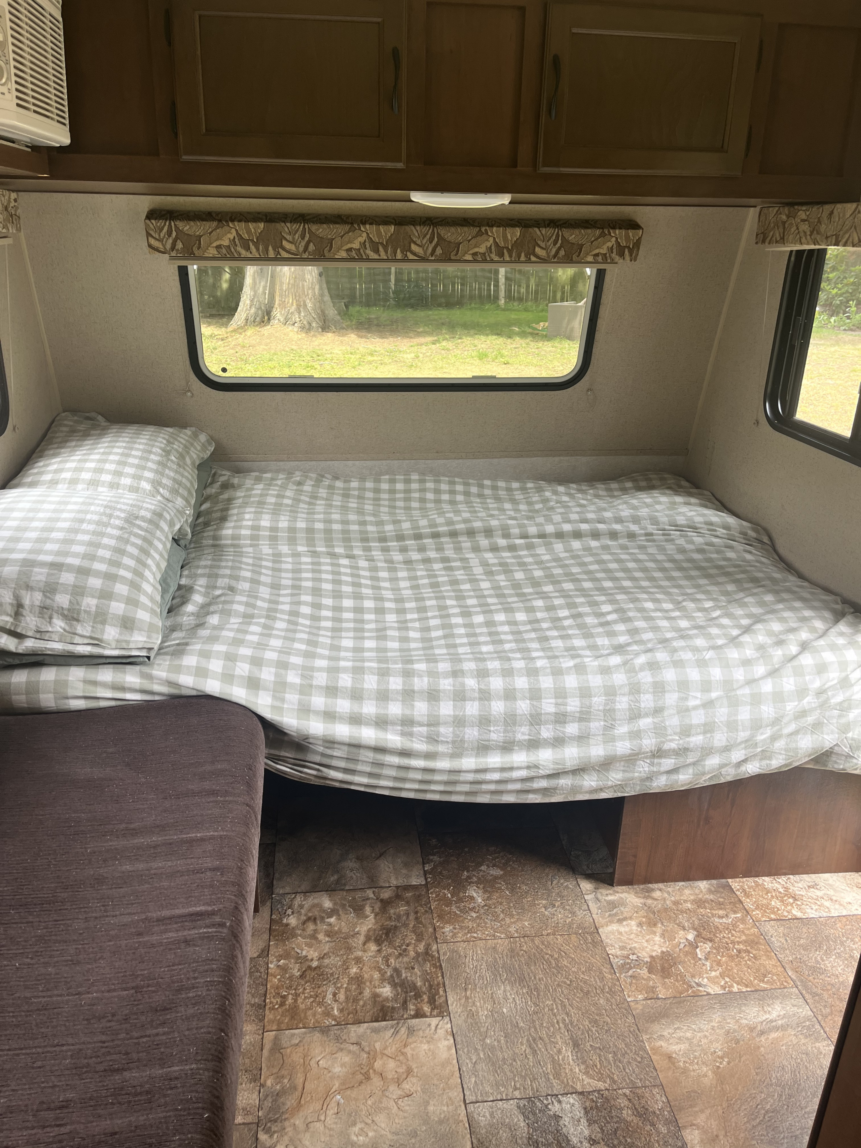 RV rental interior featuring a bed with sage green checkered bedding, nature views from windows, and wood cabinets.. Jayco Jay Flight 2015