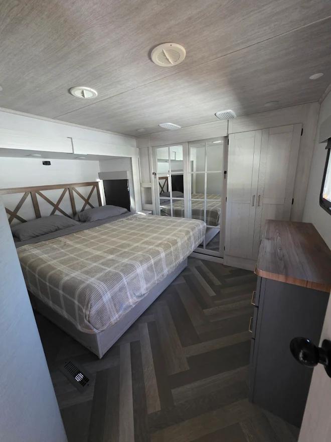 Step inside this cozy modern RV rental bedroom, featuring a plaid bed, sleek herringbone flooring, and mirrored closet.. Crusader Crusader Fifth Wheel 2024