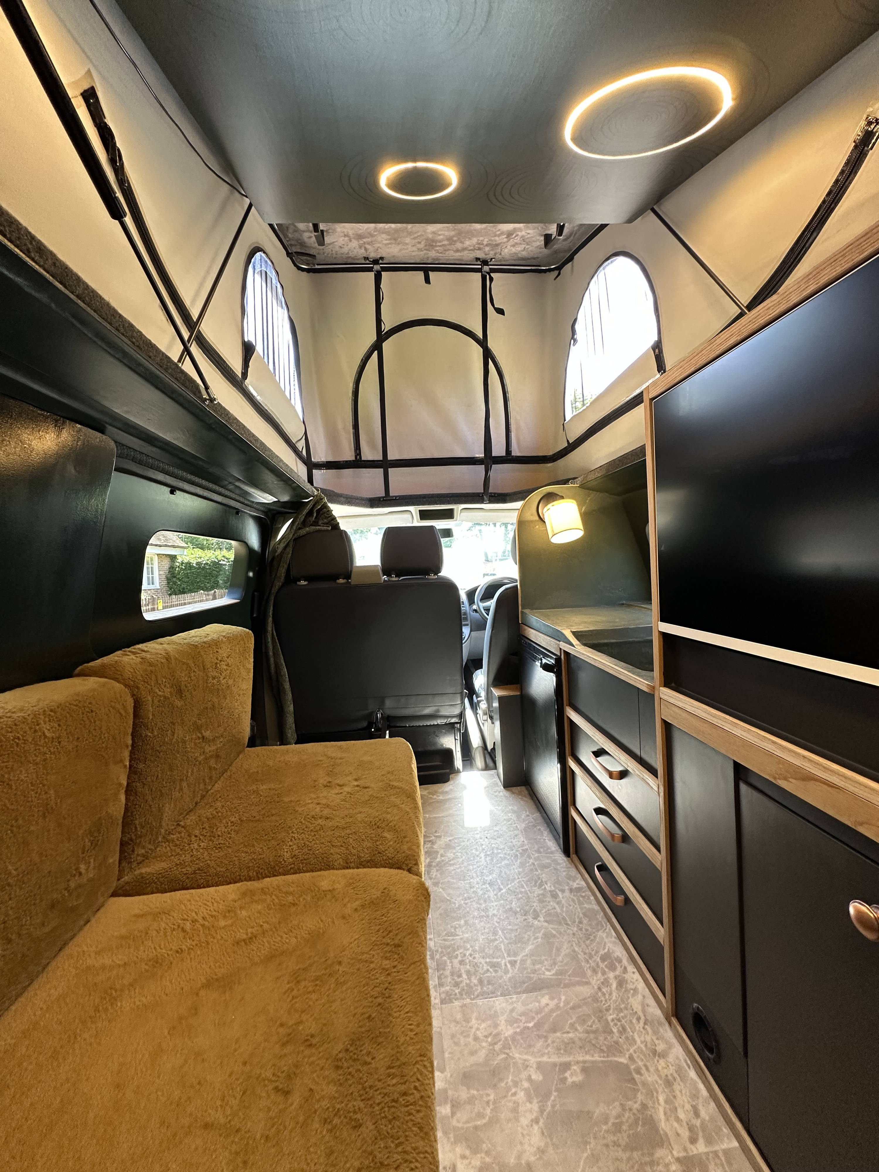 RV rental interior featuring a plush gold sofa, modern dark kitchenette, marble floor, and pop-top roof with windows and lights.. Volkswagen transporter t5.1 2012