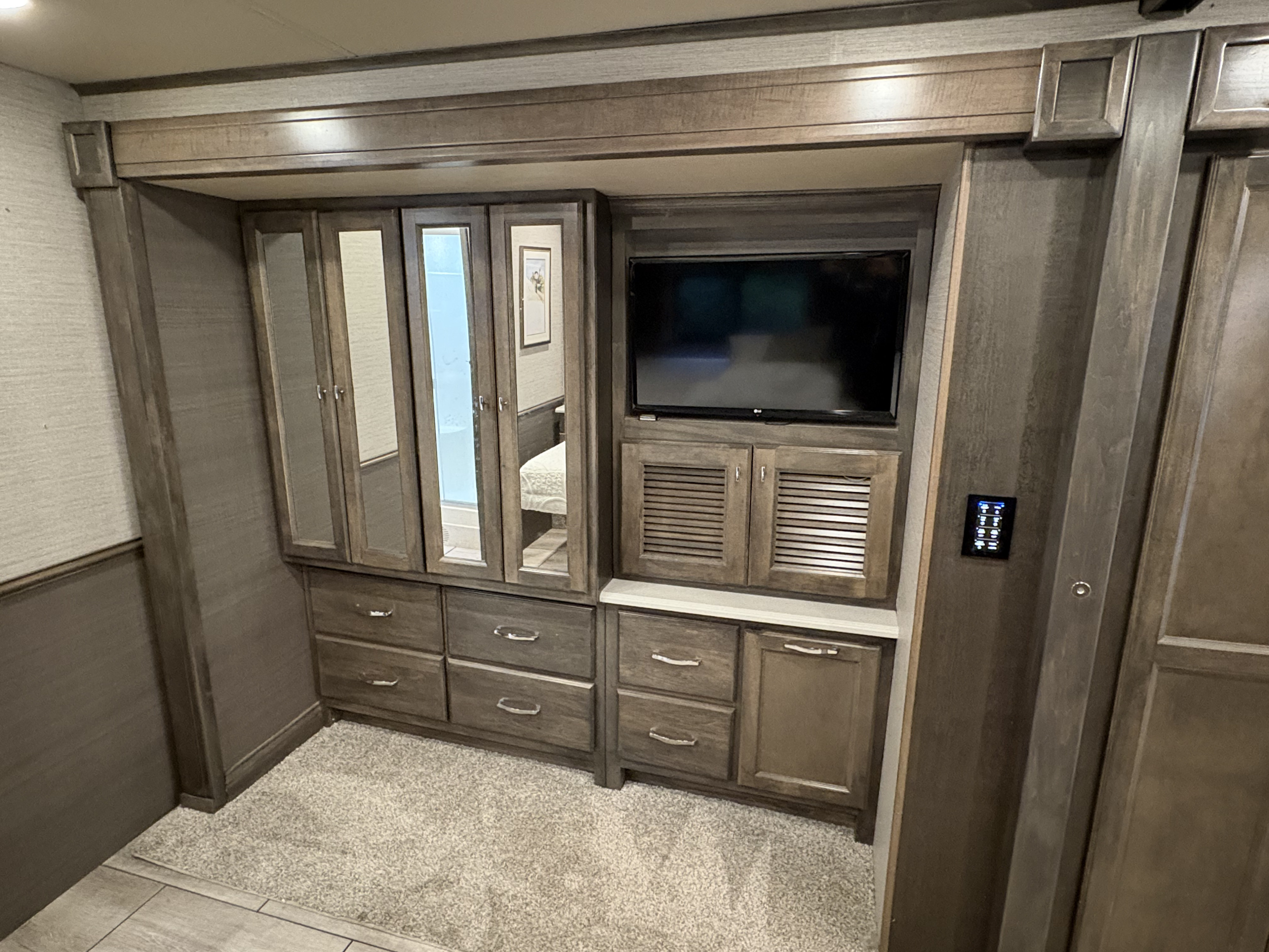 RV rental bedroom with dark wood cabinetry, mirrored closet, TV entertainment, and drawer storage for mobile living comfort.. Allegro Allegro Open Road 2022