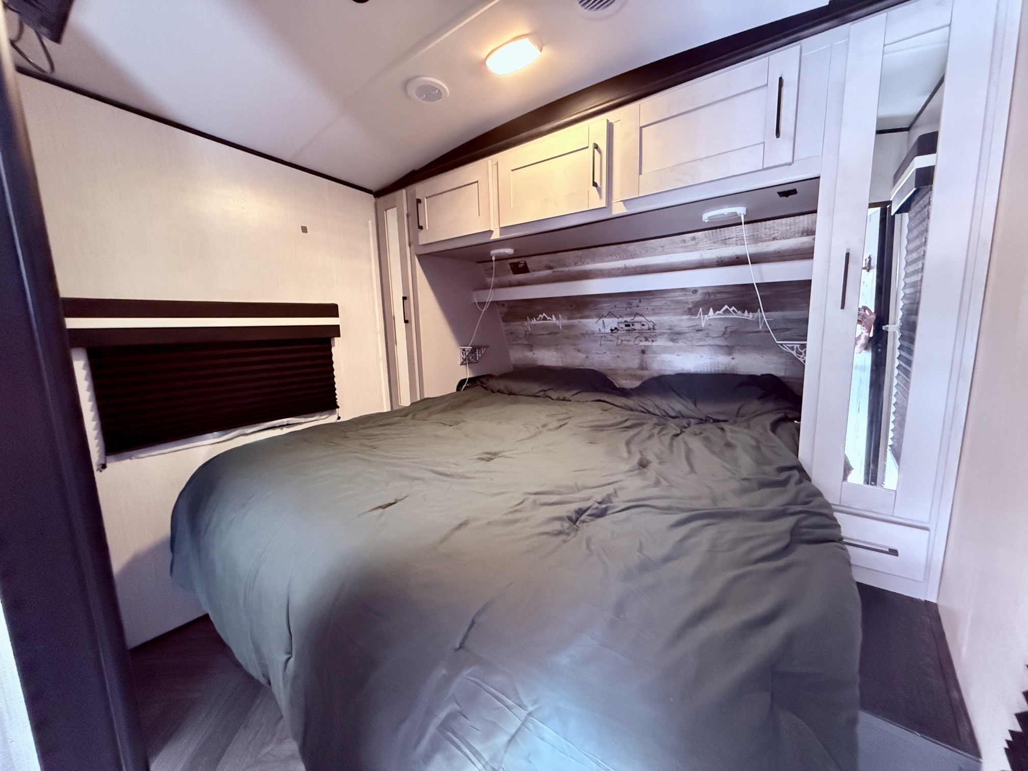 Cozy RV rental bedroom featuring a bed with dark bedding, overhead cabinets, and window blinds.. Heartland RVs Torque Toy Hauler 2022