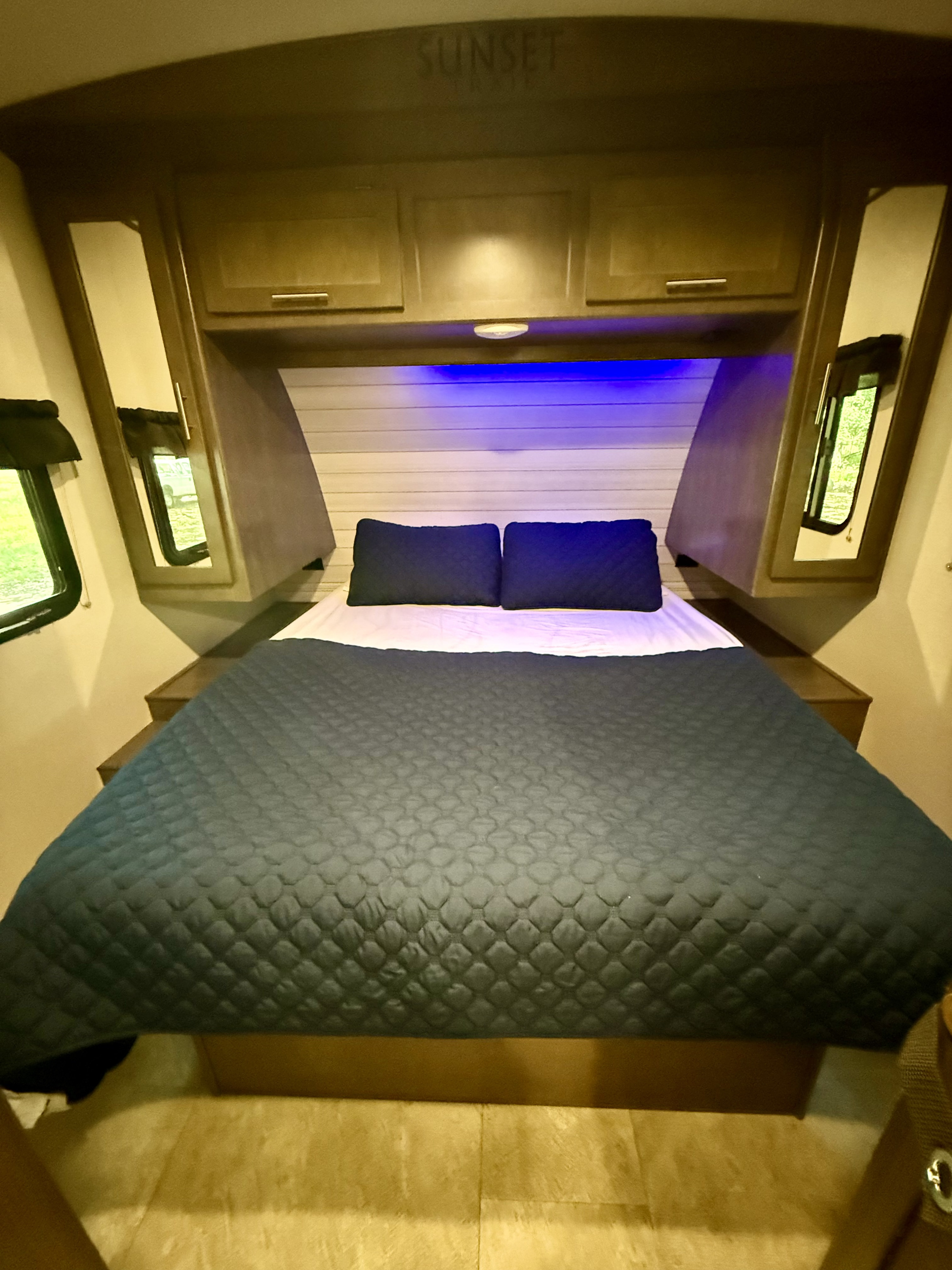 Cozy RV rental bedroom with blue accent lighting, Sunset Trail branding, overhead storage, and side windows for travel comfort.. Crossroads RV Sunset Trail Super Lite 2018
