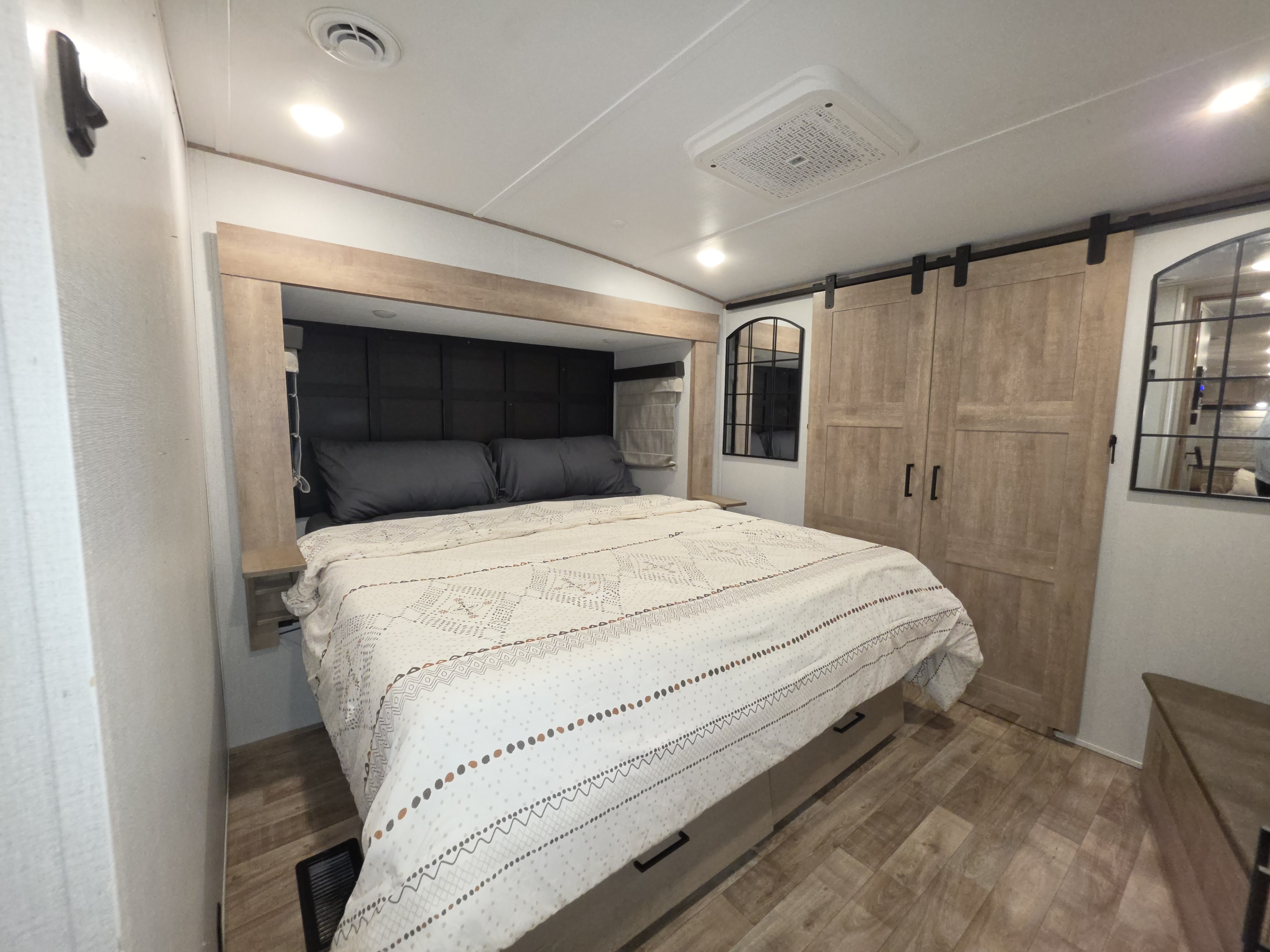 Cozy RV rental bedroom featuring a queen bed with modern patterned bedding, dark headboard, built-in shelves, and barn-style closet doors.. Keystone RV Arcadia 2022