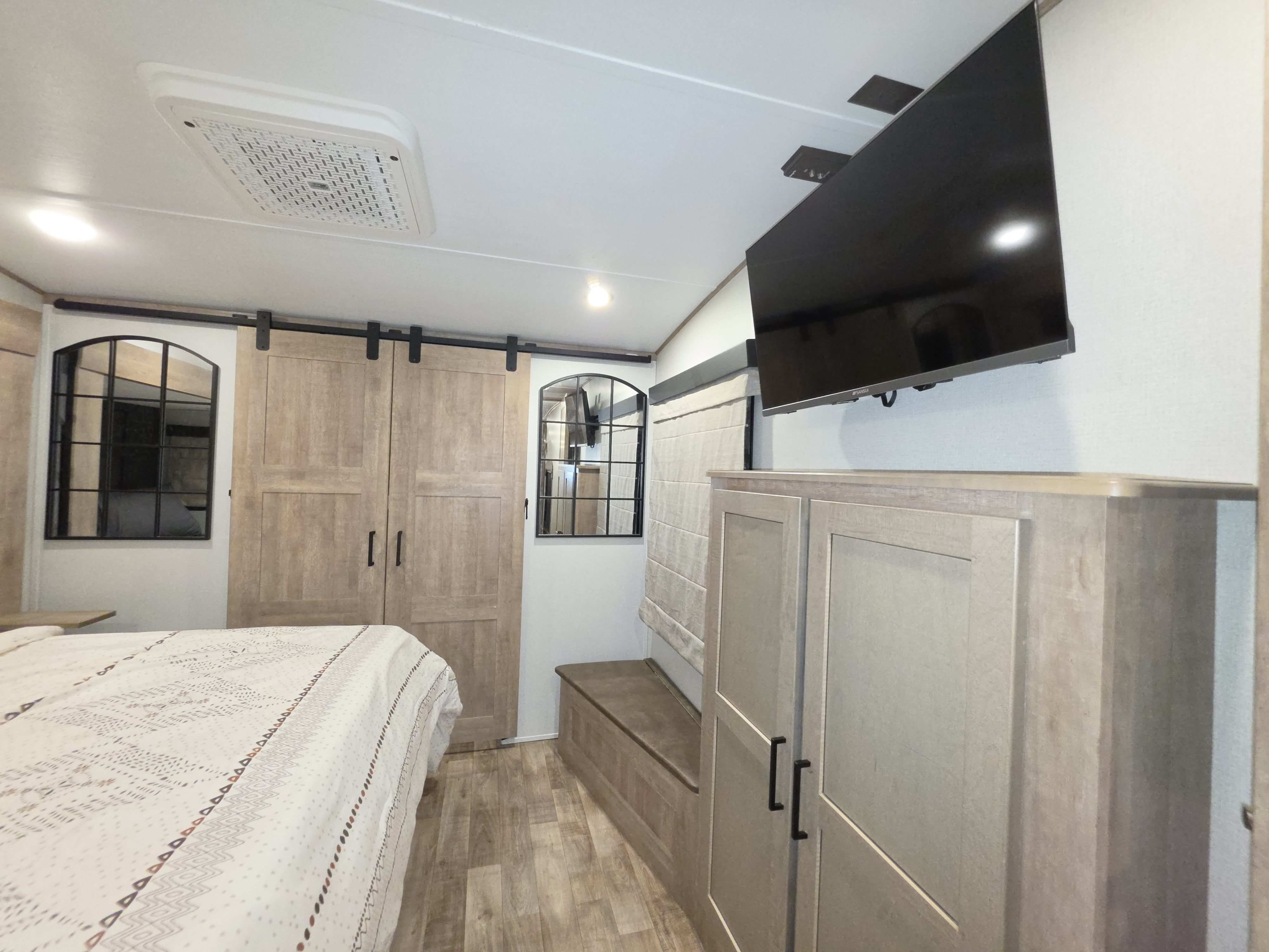 Cozy RV rental bedroom featuring barn doors, a mounted TV, and a patterned bed for comfortable travel.. Keystone RV Arcadia 2022