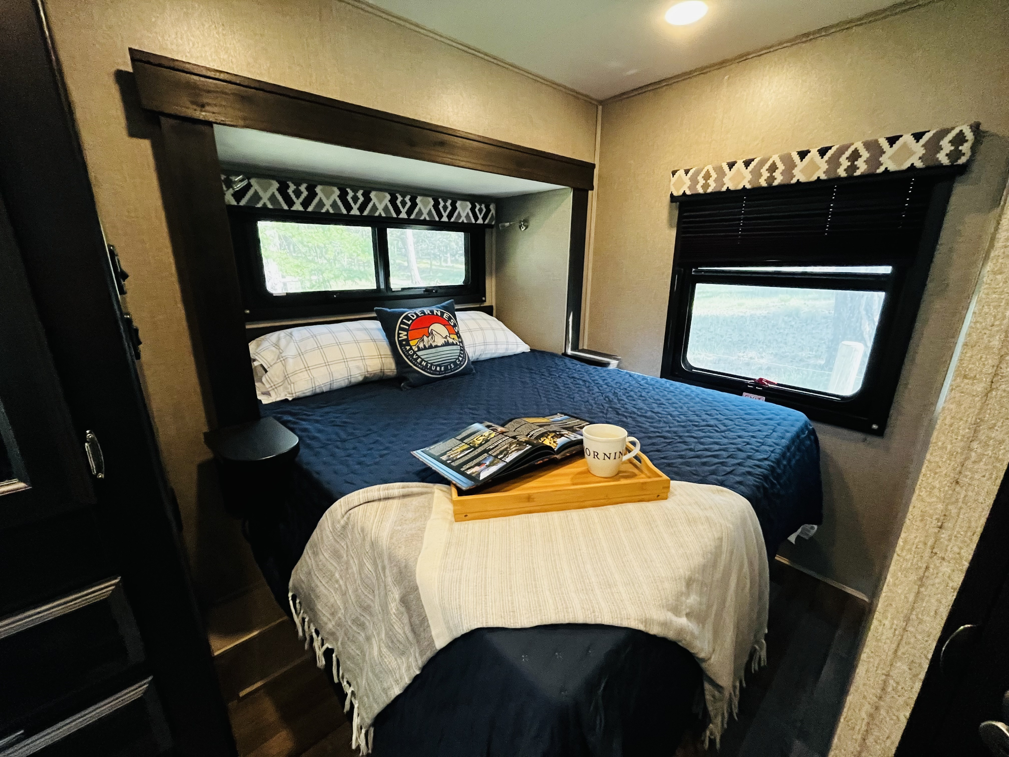 Inviting RV rental bedroom with a comfy bed, scenic window views, and a tray for morning coffee or reading.. Entegra Coach Odyssey 2021