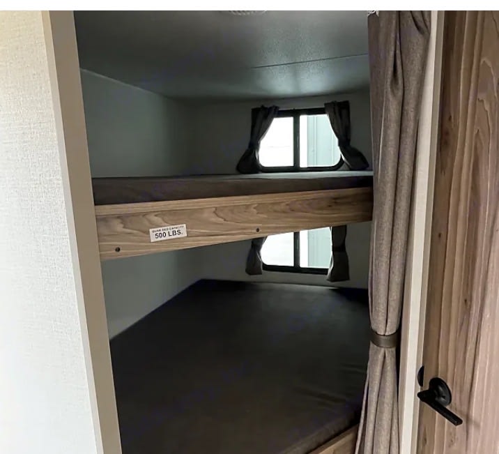 This RV rental features stacked bunk beds with mattresses, each having a small window and curtain. The top bunk is rated for 500 lbs.. KZ Connect SE 2026