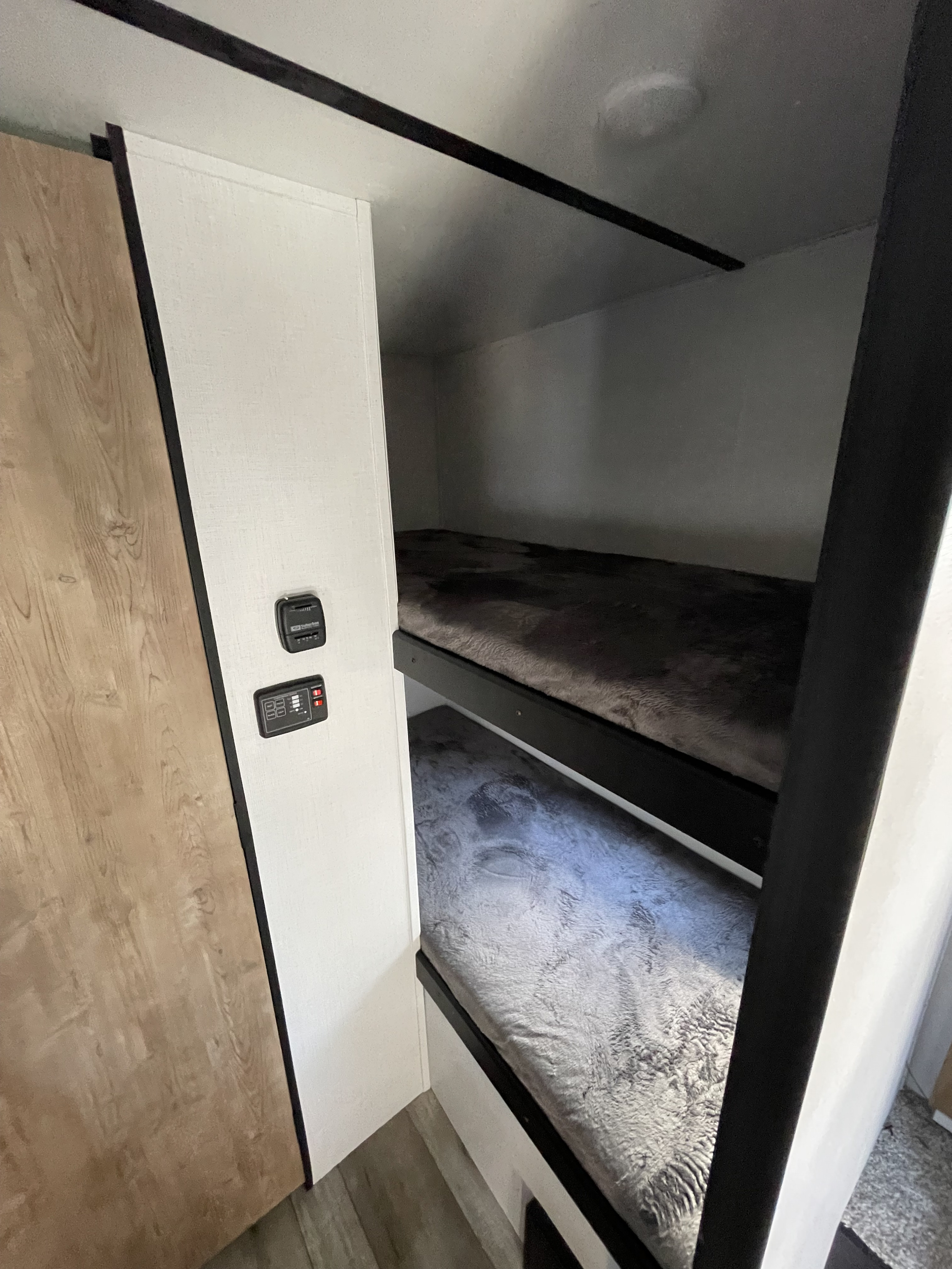 This RV rental bunk bed area features two cozy bunks with soft bedding and convenient control panels on the adjacent wall.. Keystone RV Springdale 2022