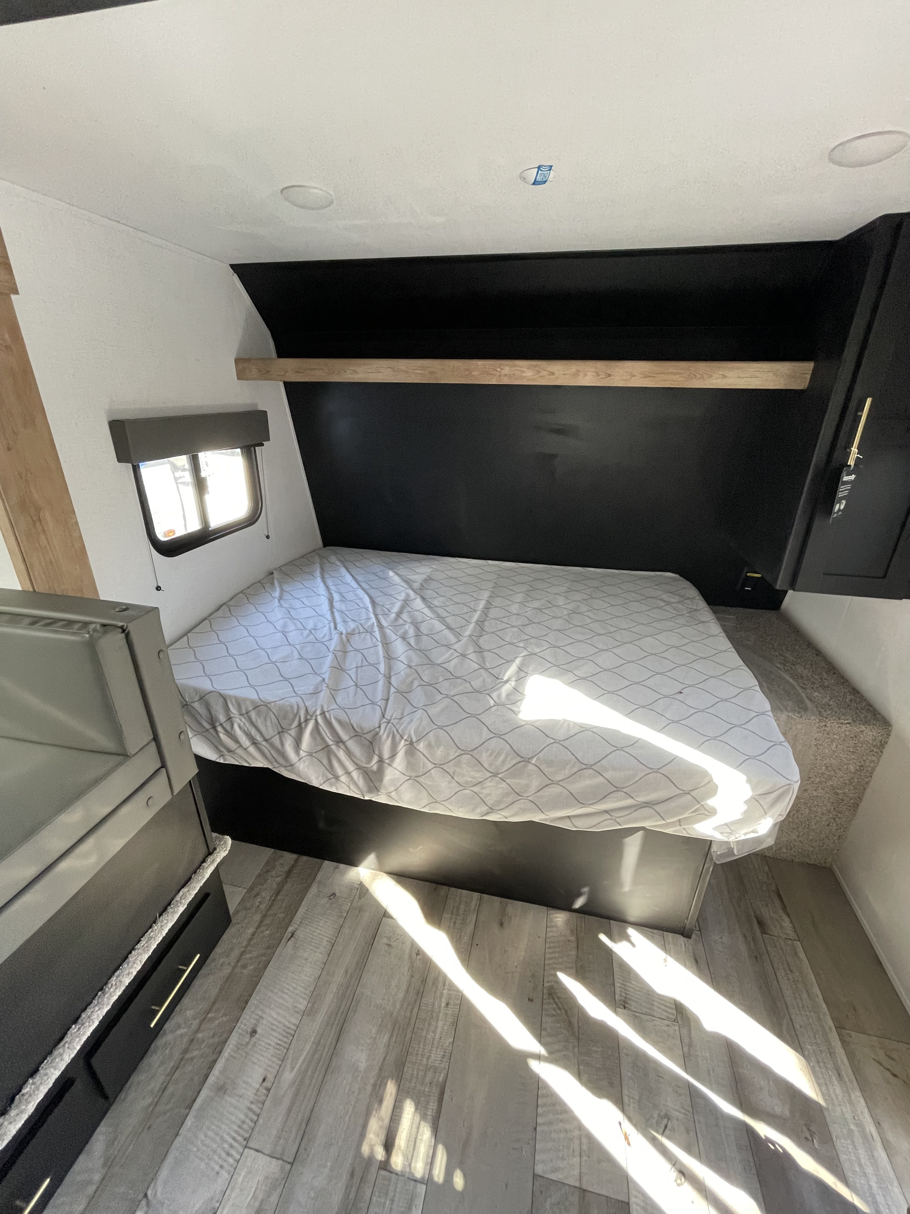 Spacious RV rental bedroom featuring a bed with patterned linens, window, storage, and wood floors. Sunlight brightens the space.. Keystone RV Springdale 2022