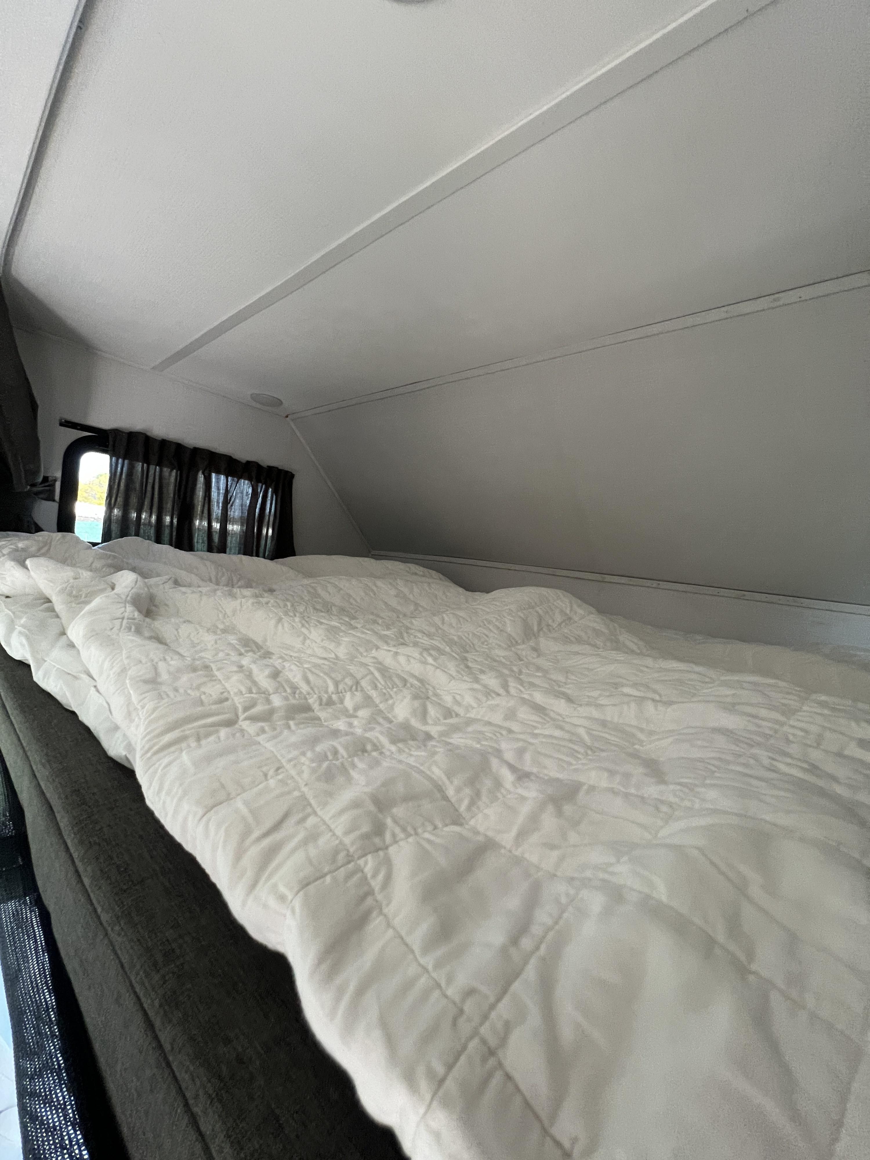 Cozy RV rental sleeping area featuring a white quilted comforter, dark curtains, and a window for scenic views.. Forest River Sunseeker Classic 2023