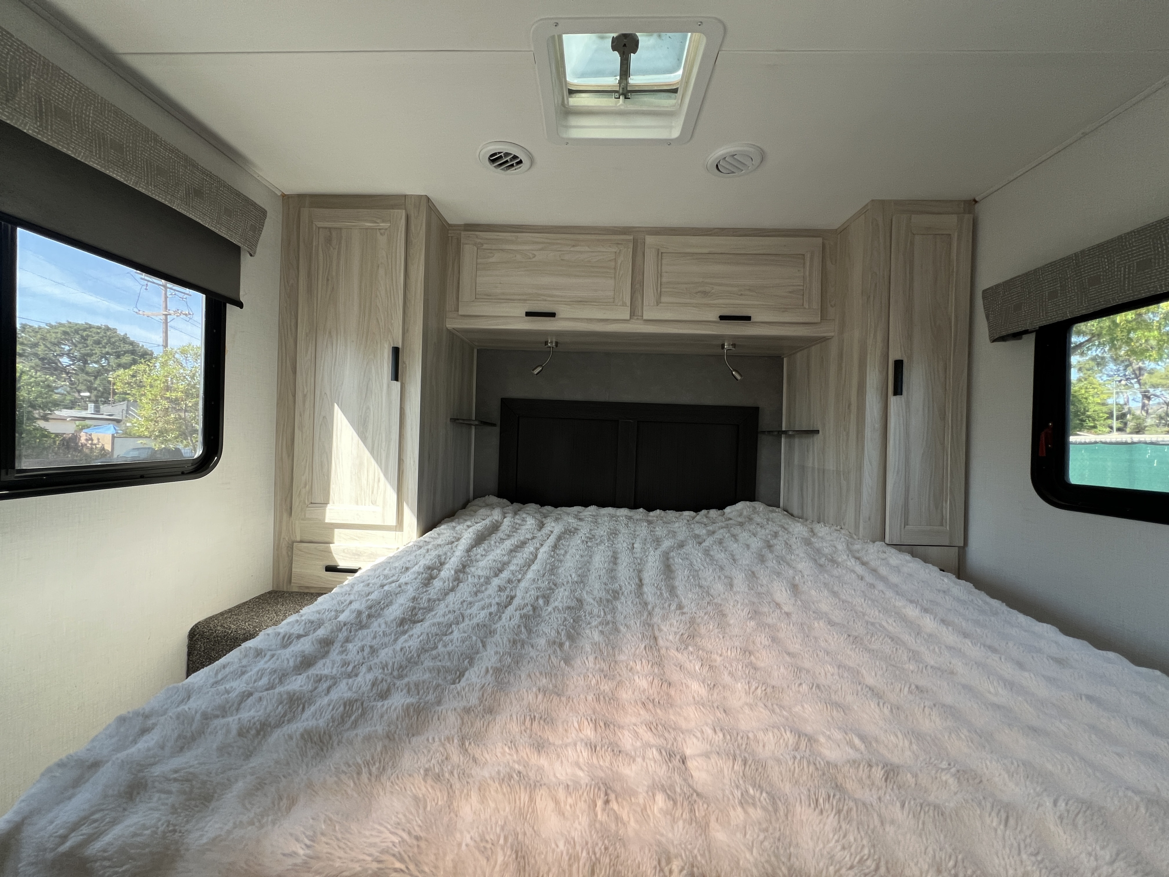 Bright RV rental bedroom, featuring a plush white bed, light wood cabinetry, and windows showing outdoor scenery.. Forest River Sunseeker Classic 2023