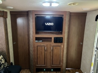 RV rental interior: Wooden entertainment center with a VIZIO TV, stereo, and storage cabinets, flanked by two brown doors.. Forest River Salem Cruise Lite 2014