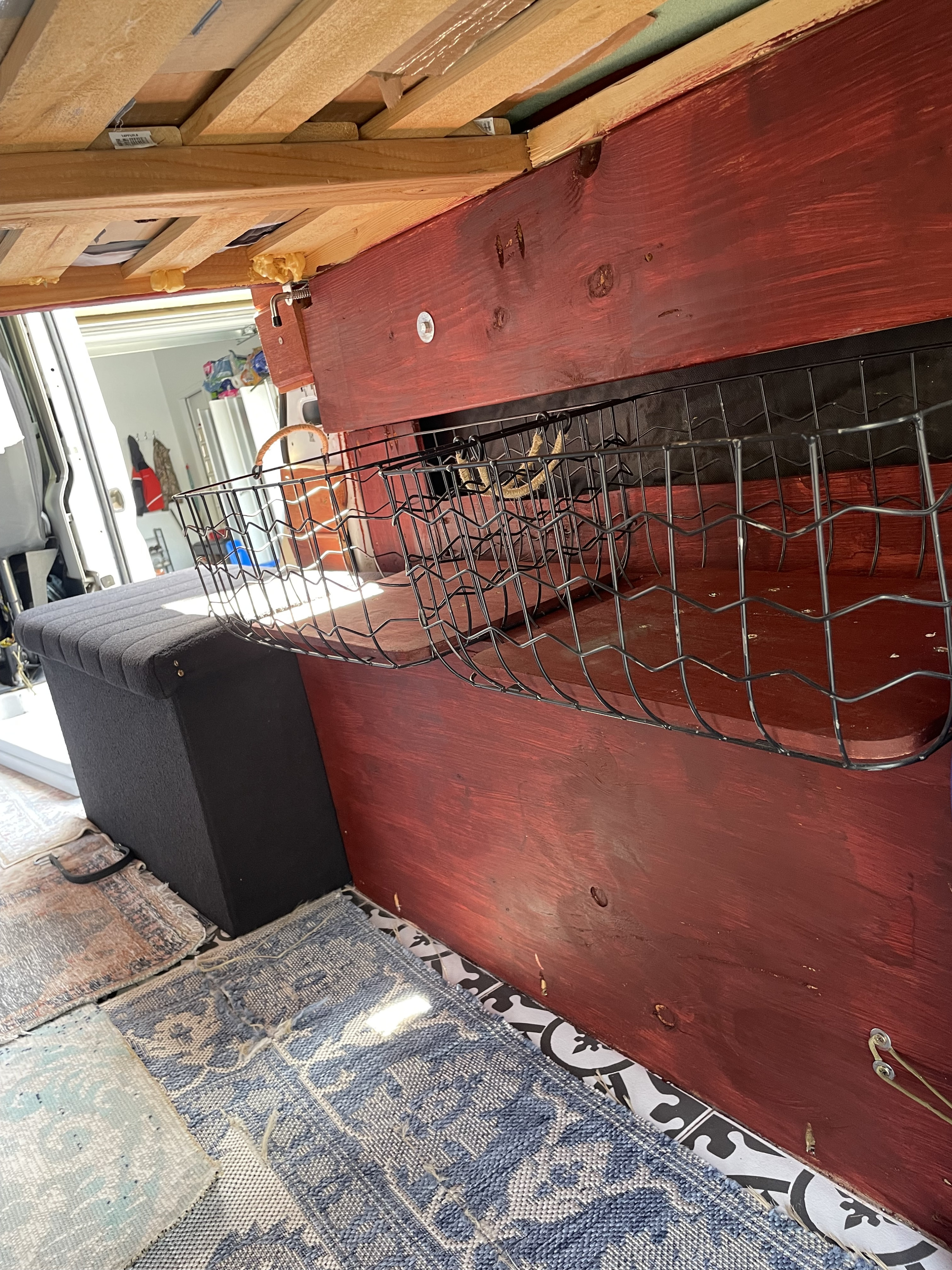 Custom RV rental interior with wooden bed frame, red storage panel, wire basket, upholstered bench, and patterned floor.. Dodge Other 2021