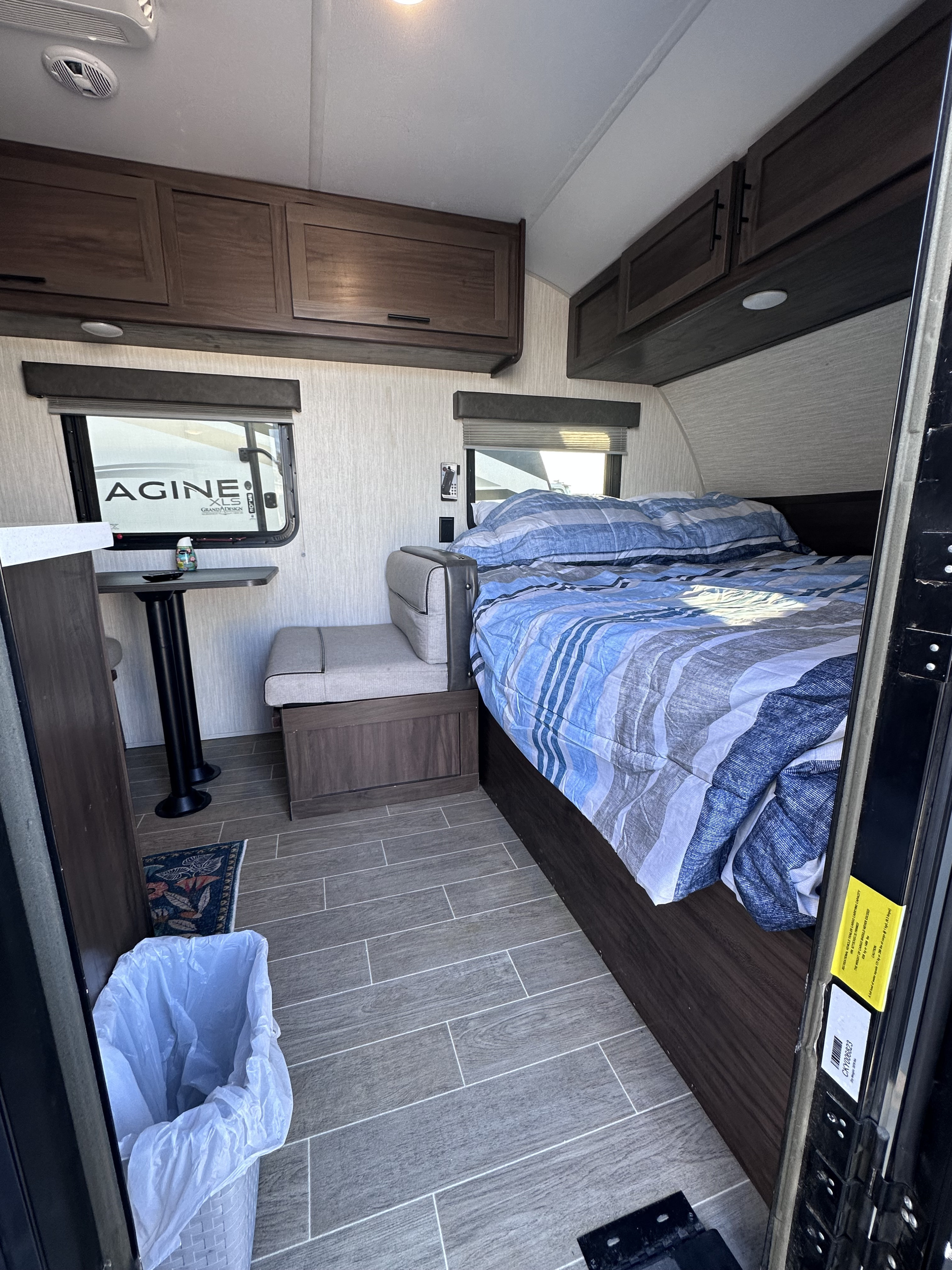 Compact rv rental interior featuring a comfy bed with blue bedding, small dinette, overhead cabinets, and wood-look floor.. Forest River Cherokee Wolf Pup 2020