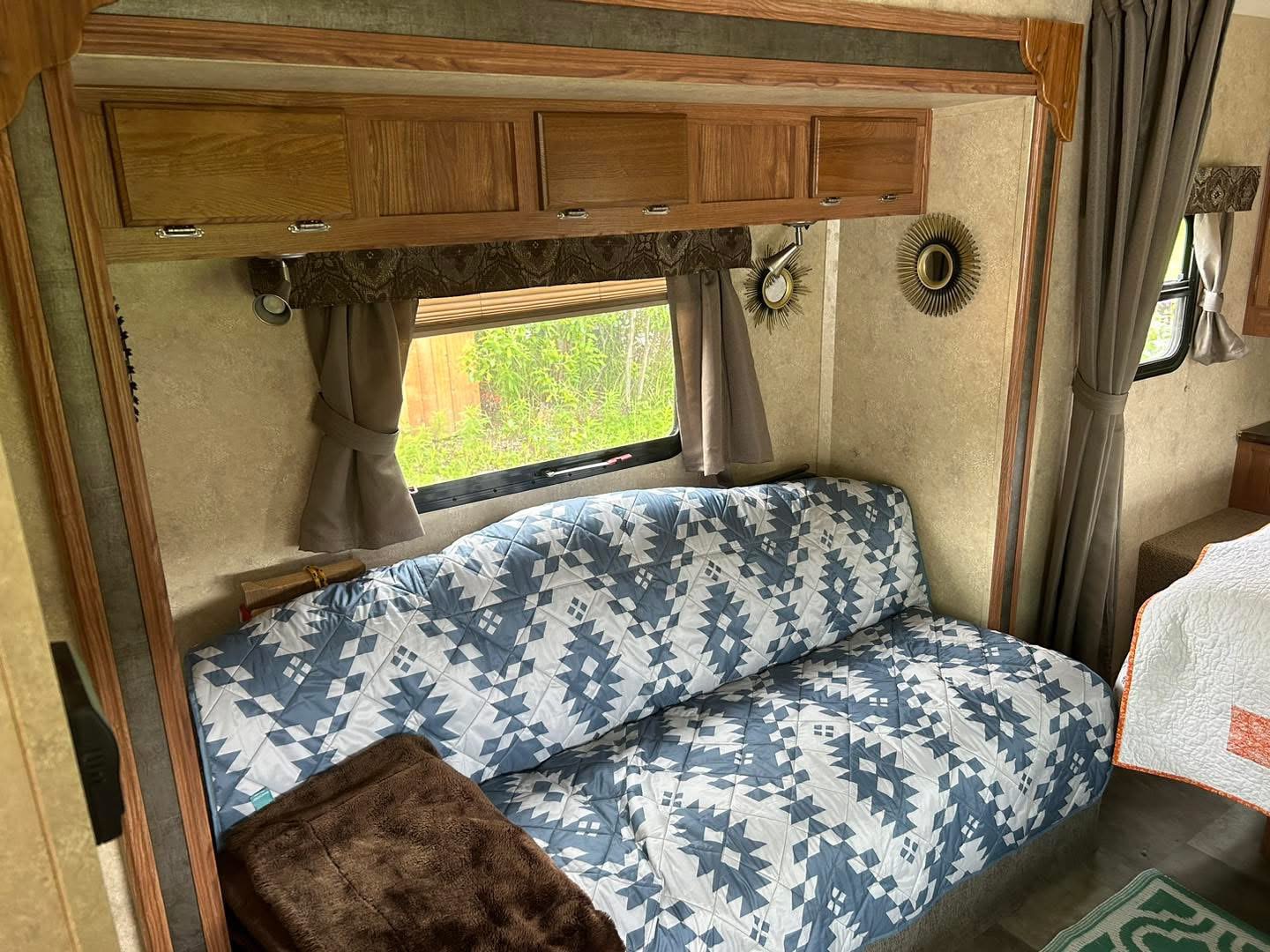 Cozy RV rental living space with a blue patterned sofa, window view, and wooden overhead storage.. Forest River Flagstaff Micro Lite 2014