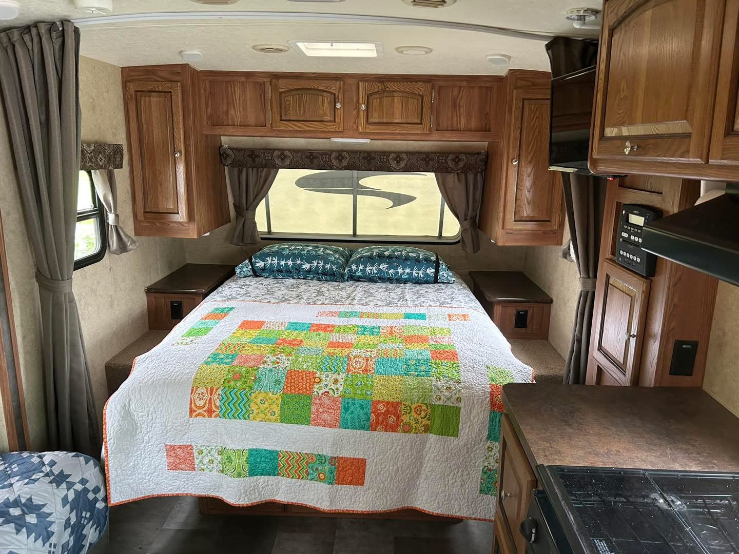 Cozy RV rental bedroom with a colorful patchwork quilt, wooden cabinets, side windows, and a view of the kitchen.. Forest River Flagstaff Micro Lite 2014