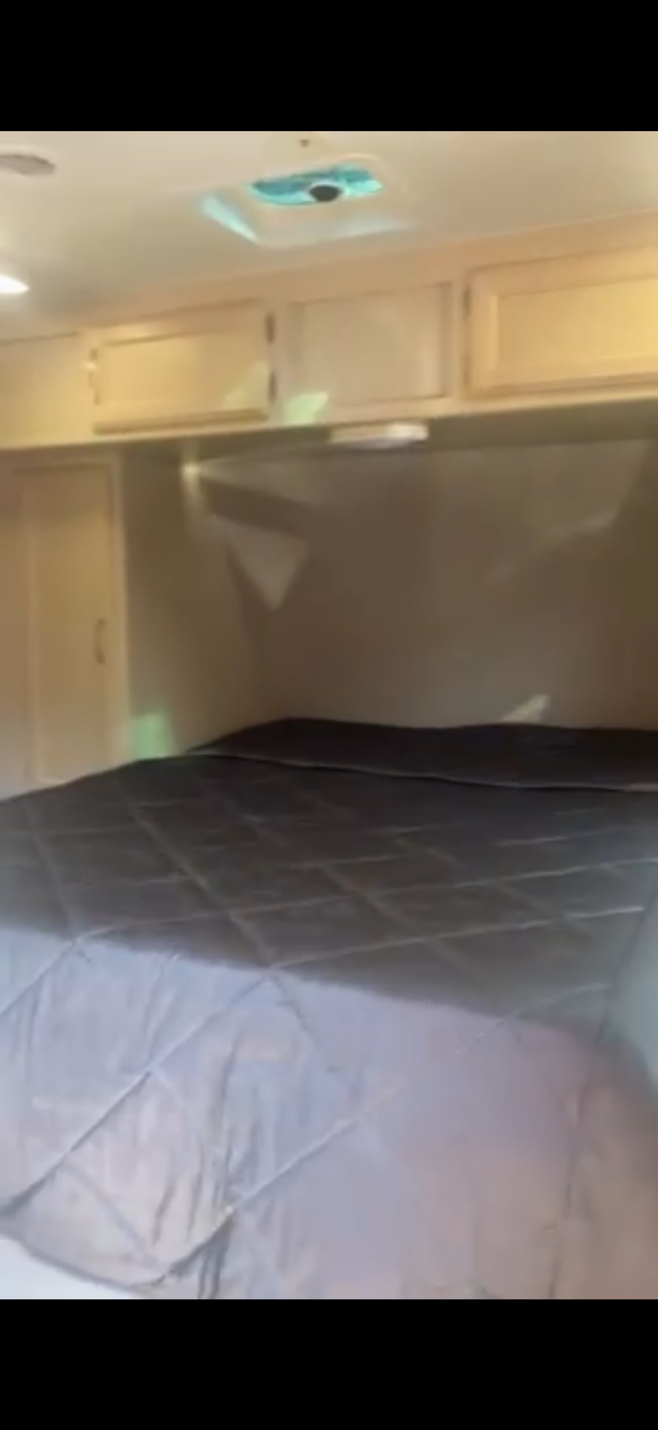 Inside an RV rental: a cozy bedroom with a quilted gray bed, light wooden overhead cabinets, and a ceiling vent.. Winnebago 2500RL 2018