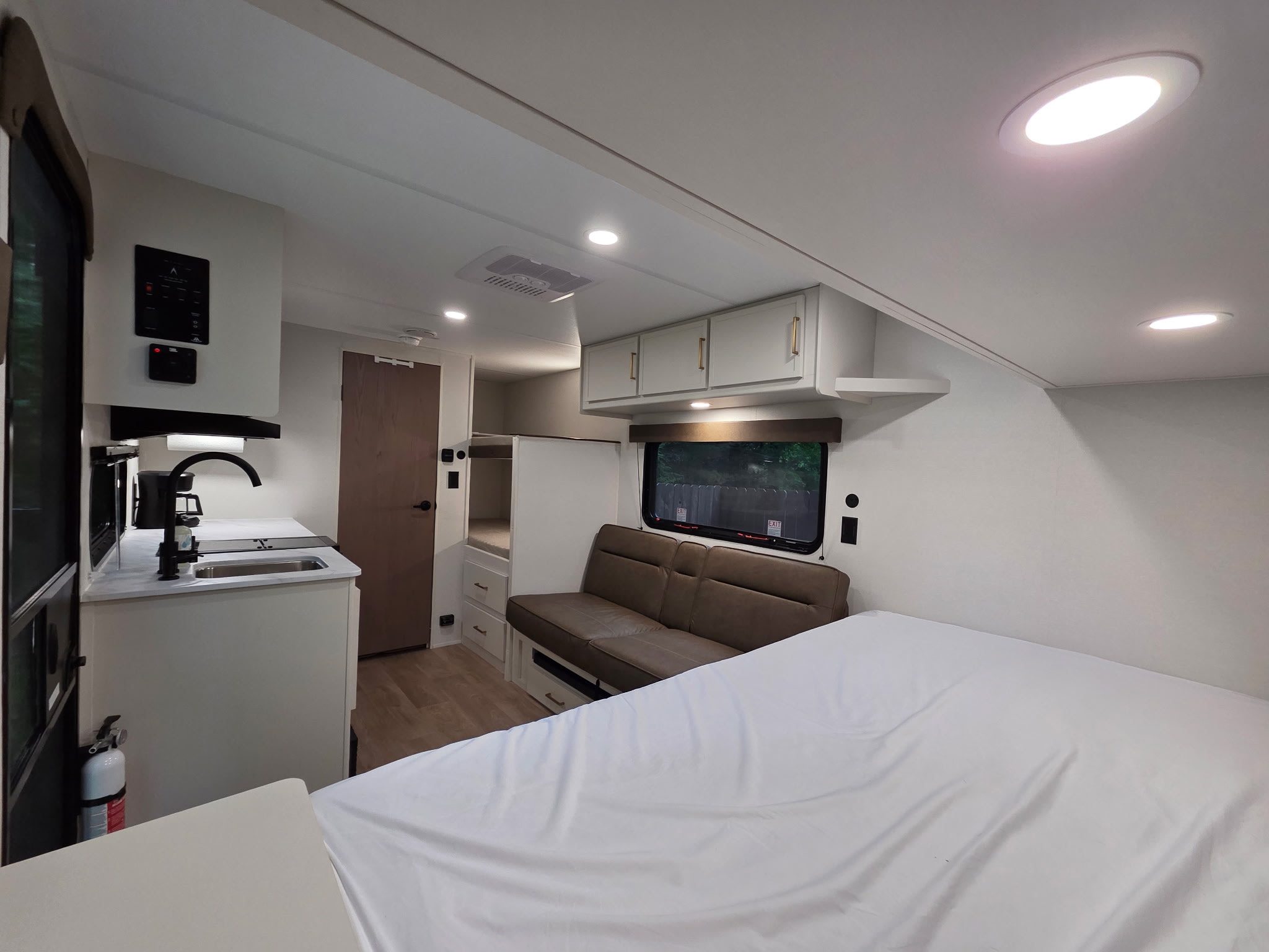 Modern RV rental interior: a comfy bed, kitchen counter with sink, and sofa in a well-lit, compact space.. Grand Design Transcend One 2026