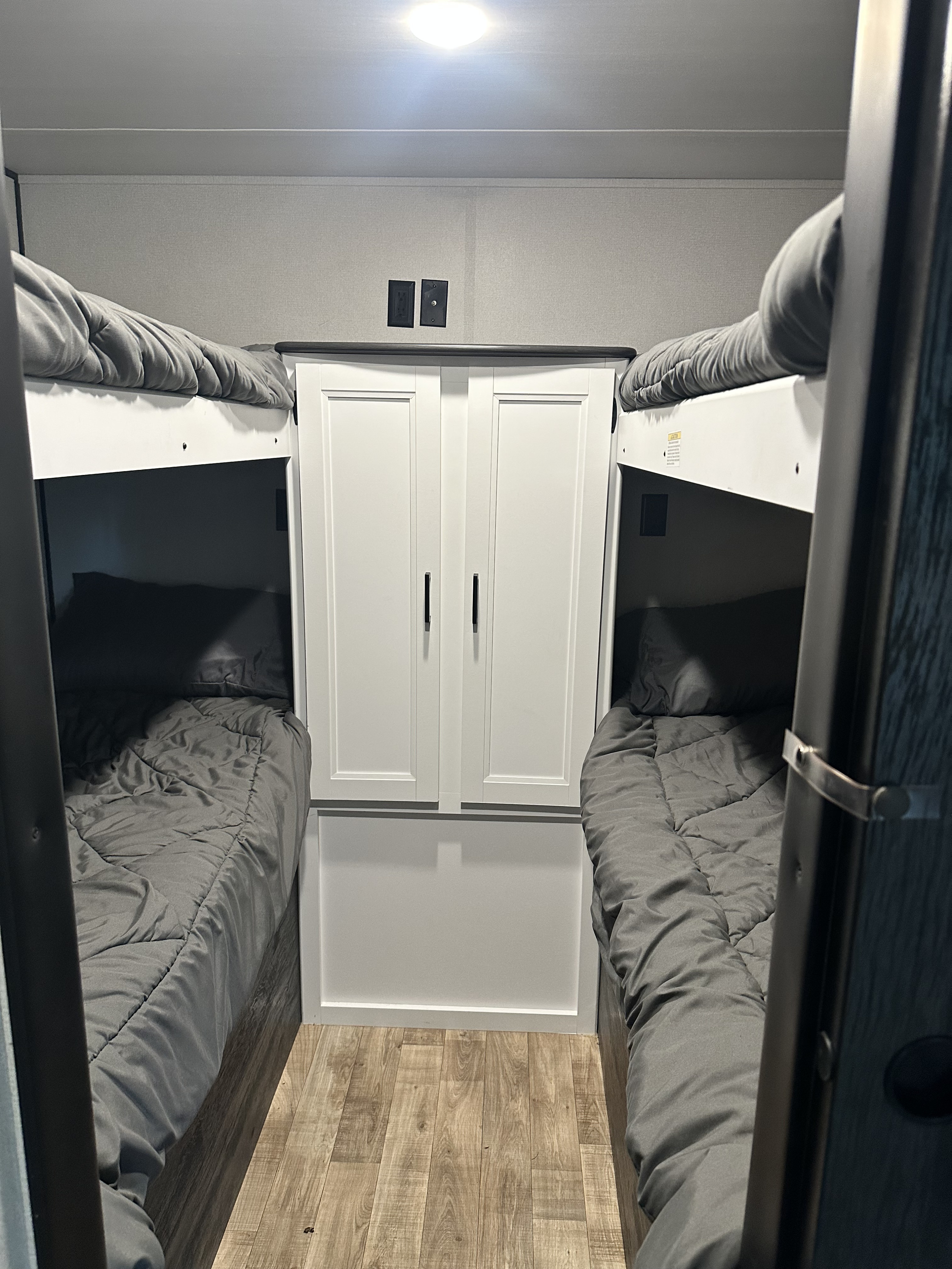 RV rental bunk bed area featuring two sleeping berths with gray bedding, a central white cabinet, and power/TV outlets.. Keystone RV Hideout 2022