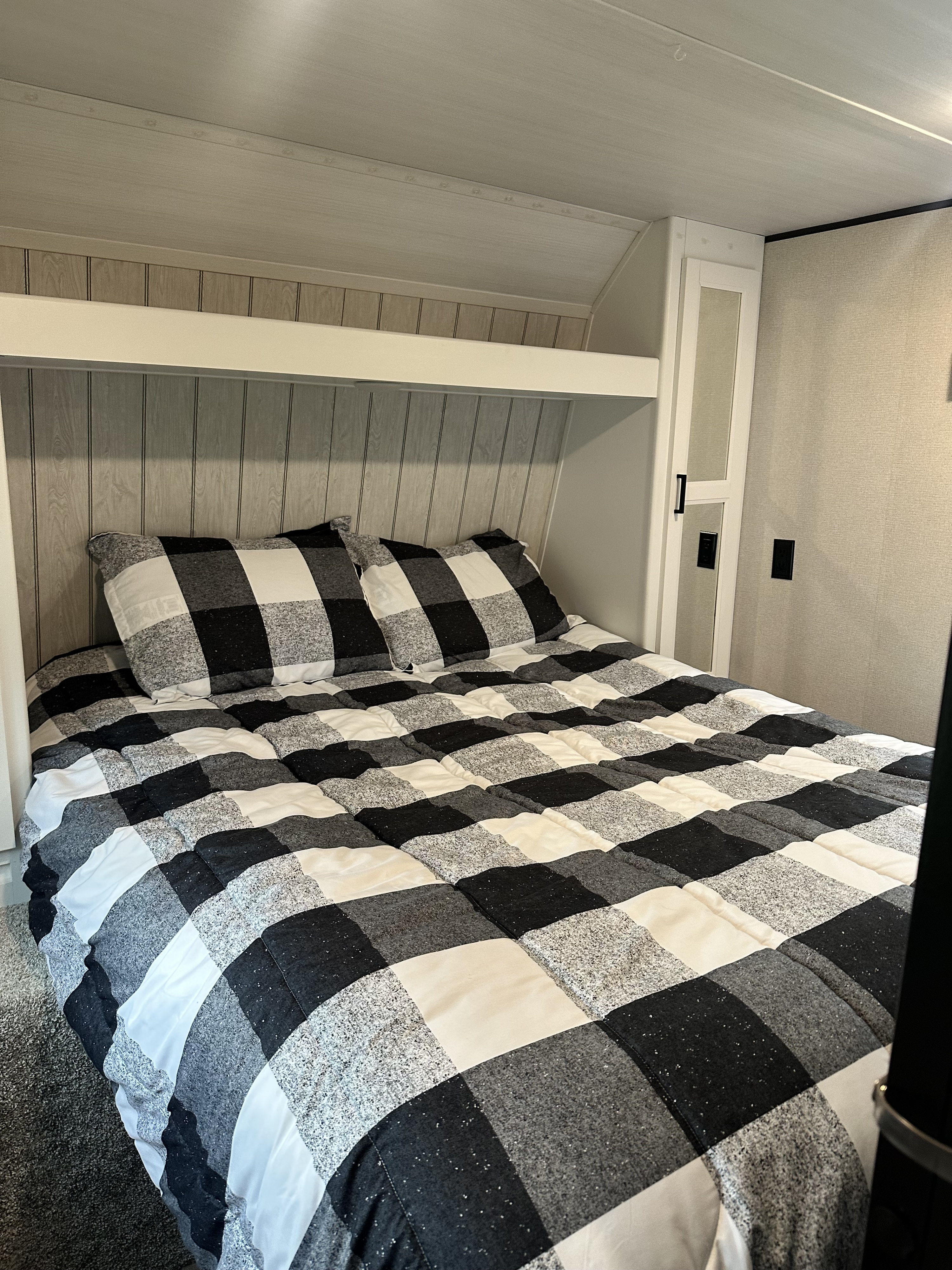 Cozy RV rental bedroom featuring a black, white, and gray checkered bed, built-in storage, and paneled headboard.. Keystone RV Hideout 2022