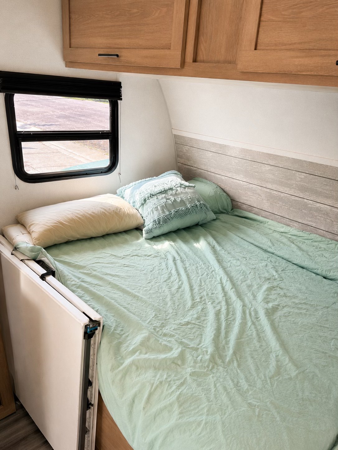 Cozy RV rental bedroom with mint green bedding, window, and wooden cabinets, offering a compact travel space.. Forrest River Primetime Avenger 2024