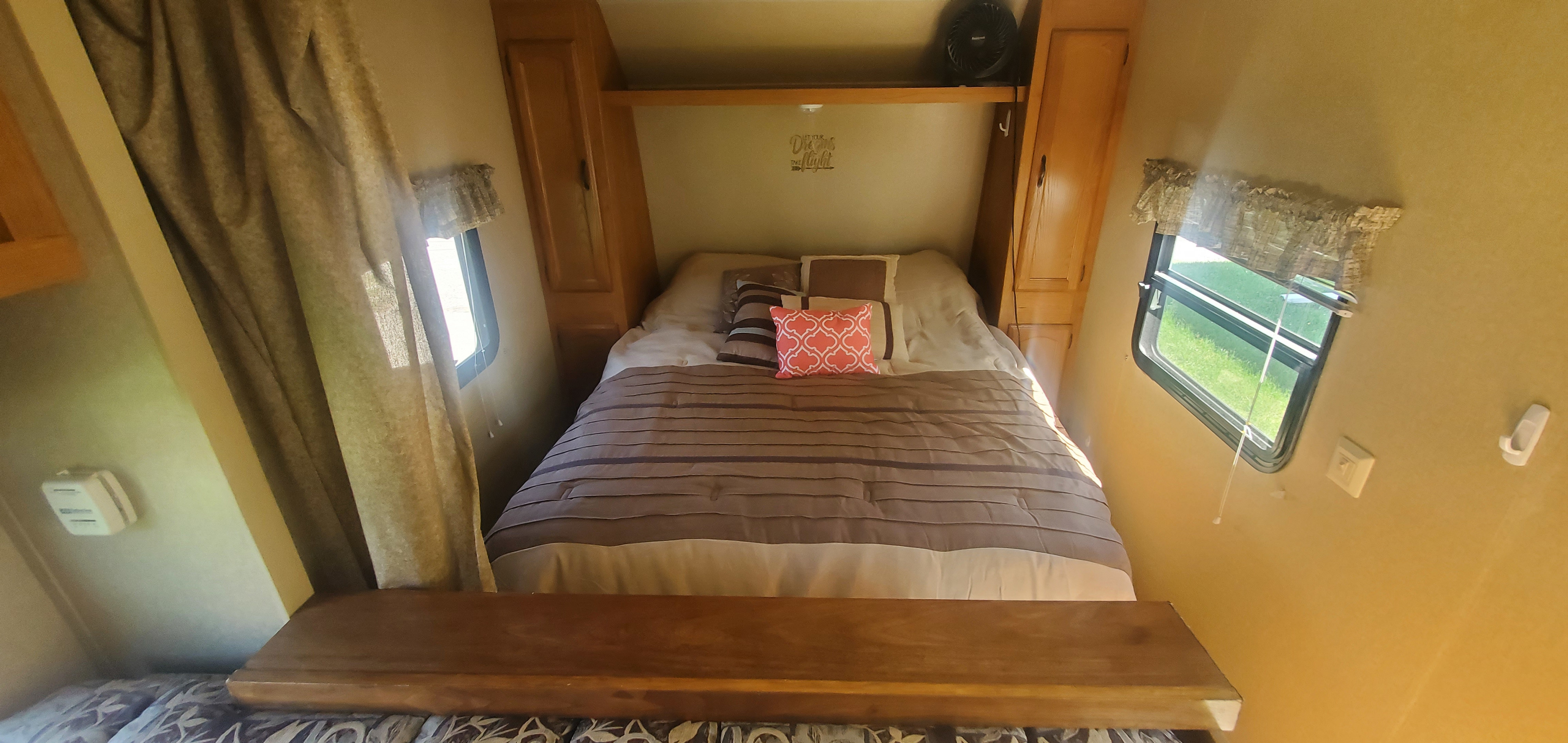 RV rental bedroom: cozy bed with striped comforter, overhead storage, and windows for light.. Forest River Wildwood X-Lite 2011