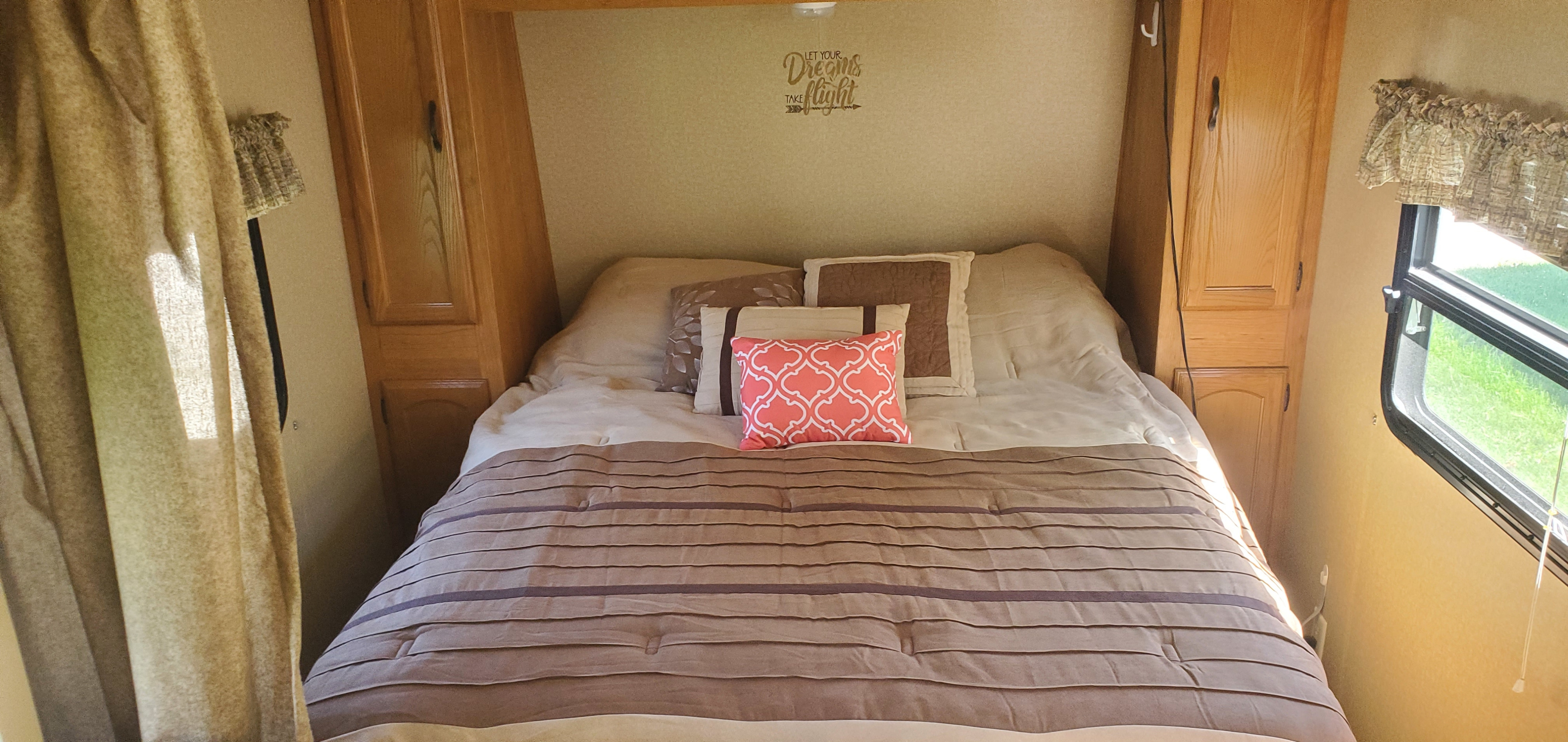 An inviting RV rental interior: a neatly made bed with brown/tan bedding, patterned pillows, and wood cabinetry.. Forest River Wildwood X-Lite 2011