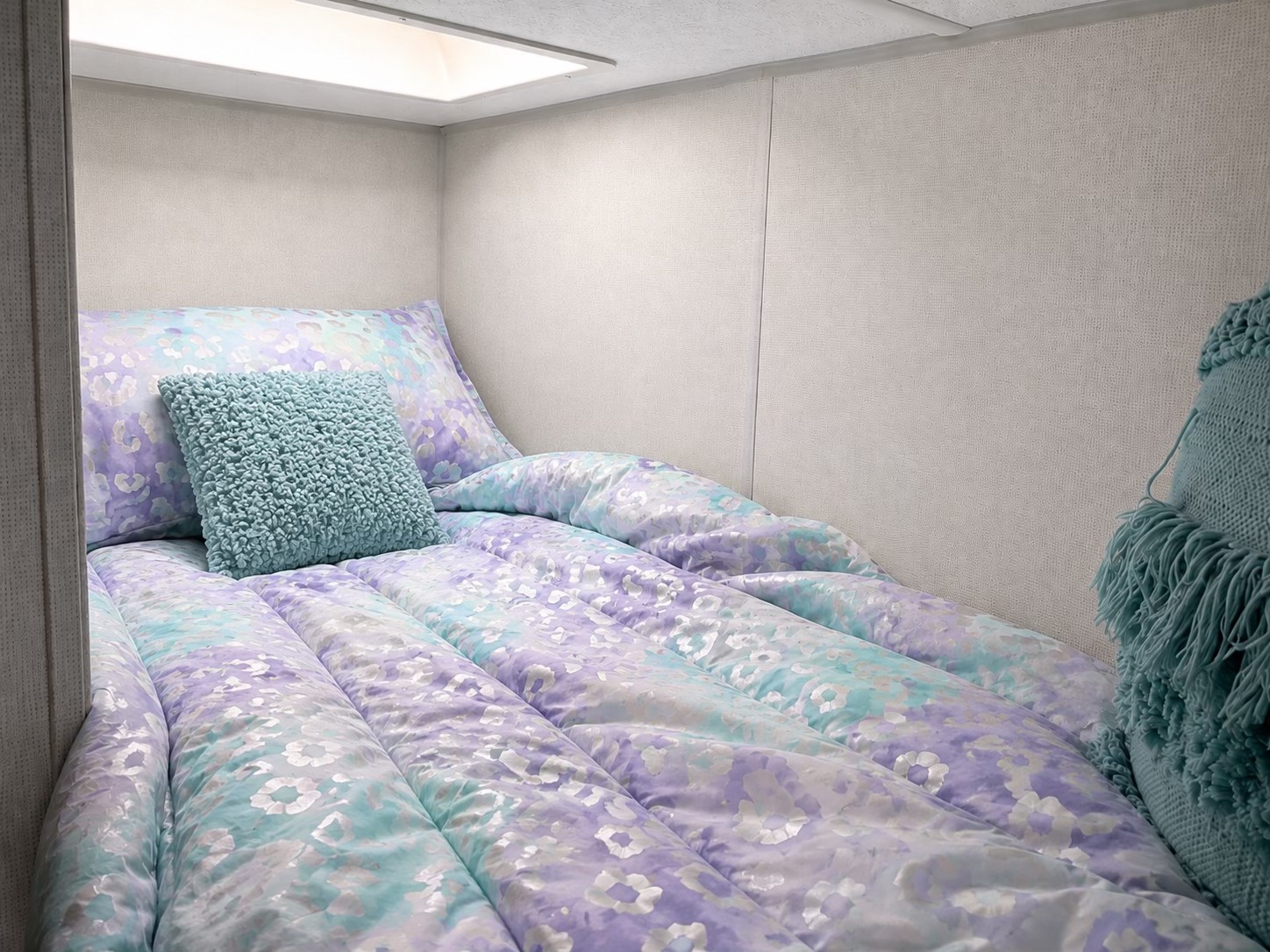 Cozy RV rental bunk bed with pastel patterned bedding and a teal textured pillow, perfect for a restful sleep.. Forrest River Primetime Avenger 2024