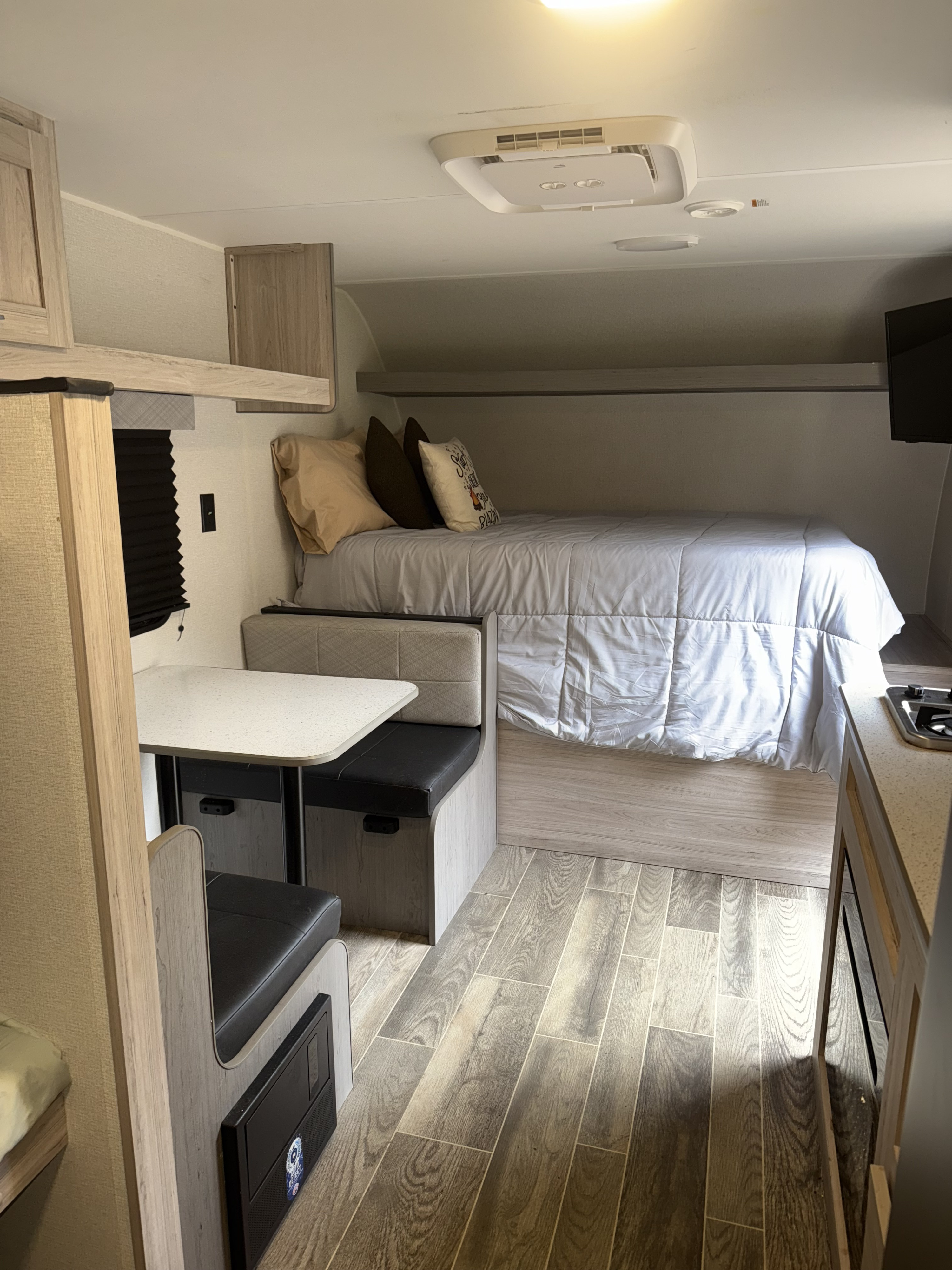 Cozy rv rental interior featuring a bed, dinette, kitchen counter, and wood-look flooring under soft lighting.. Heartland RVs Pioneer 2025