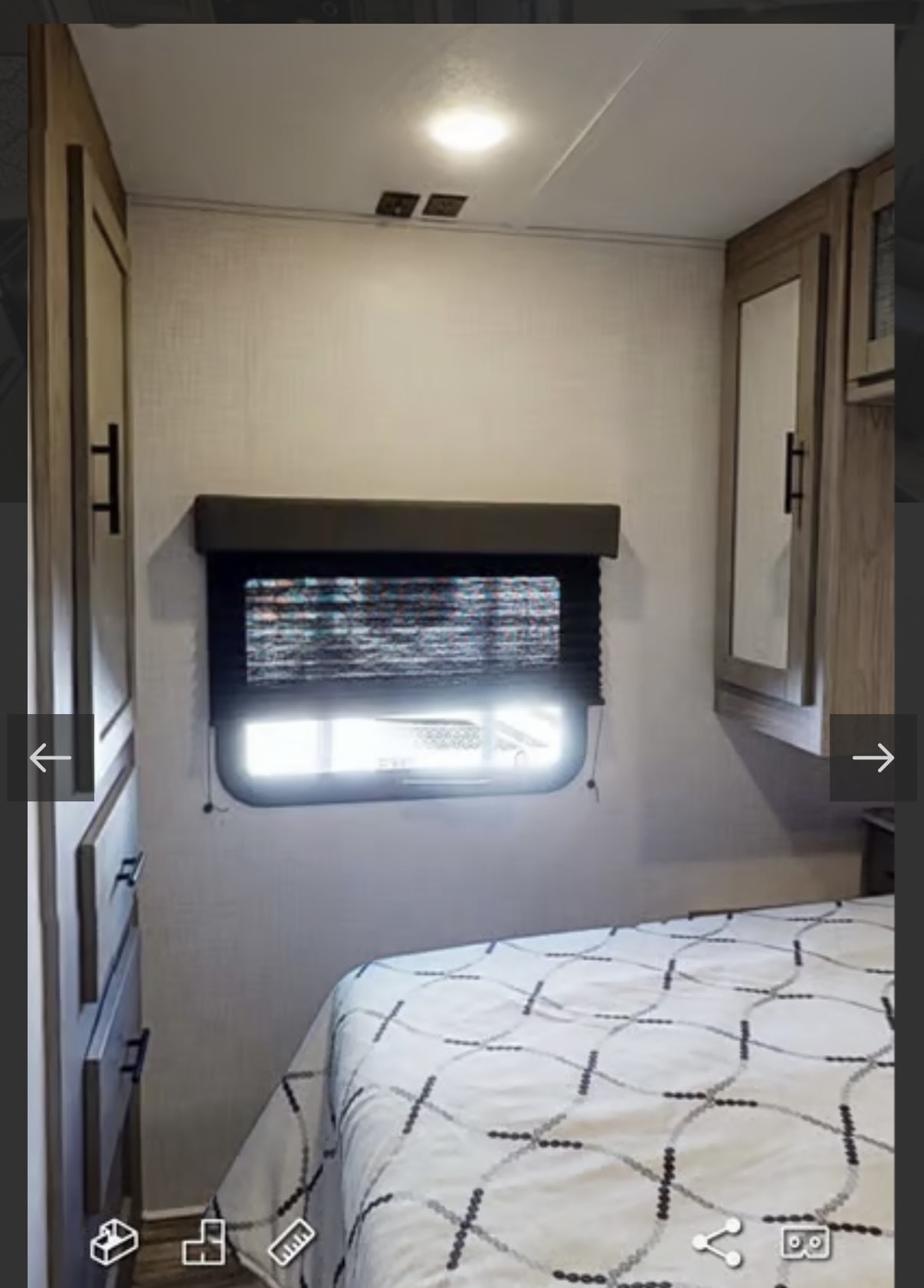 Interior of an RV rental bedroom showing a bed, window with blind, and wooden cabinets. Comfort for travel.. Keystone RV 2955RL 2022