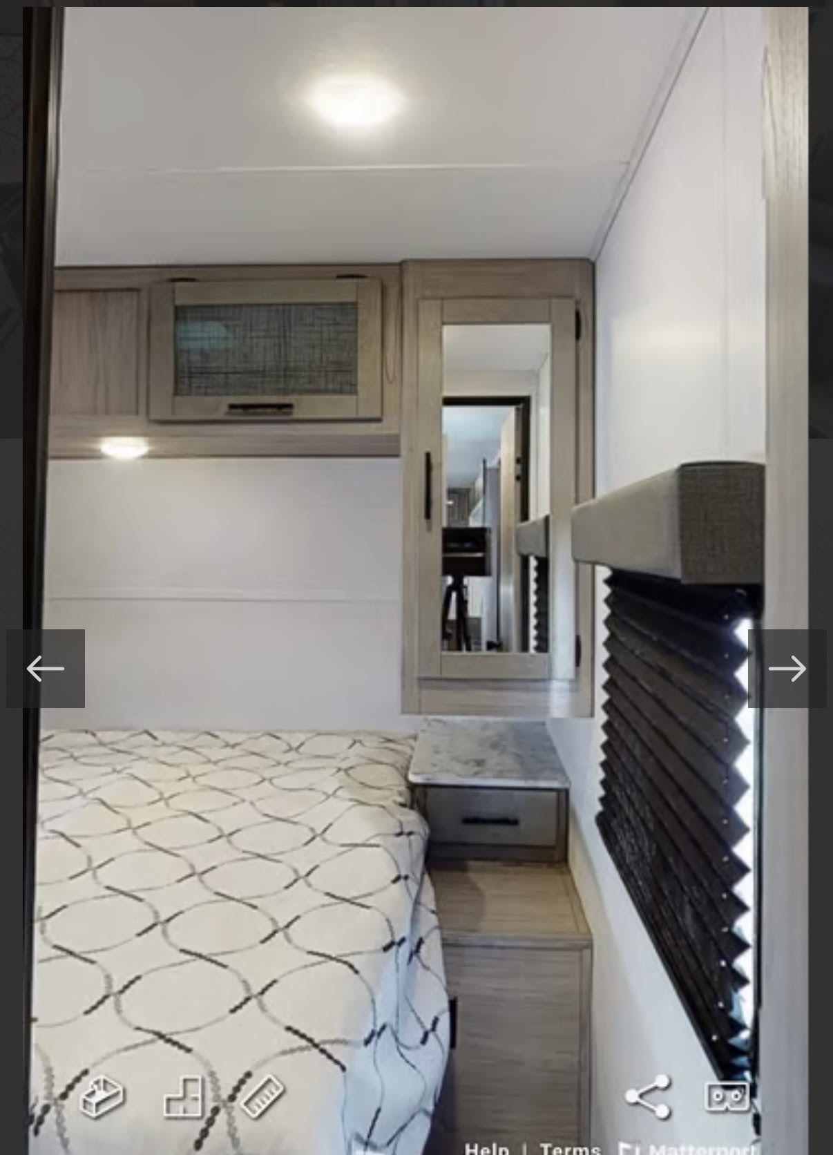 Cozy RV rental bedroom with a patterned bed, overhead cabinets, a mirror, and window blinds.. Keystone RV 2955RL 2022
