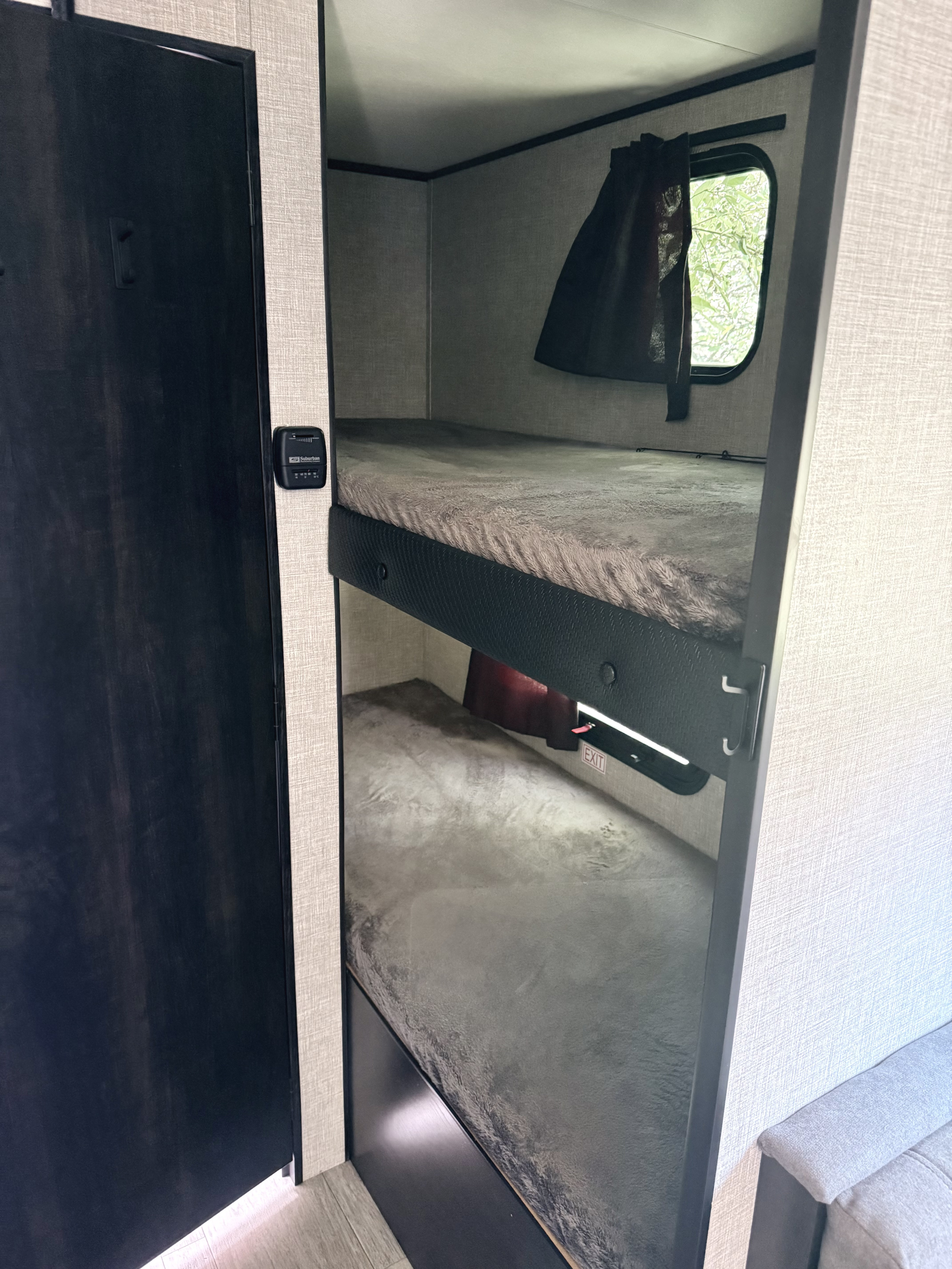 RV rental bunk beds: two sleeping areas with a window view of trees, thermostat, and a dark entry door on the left.. Jayco Jay Flight SLX 2022
