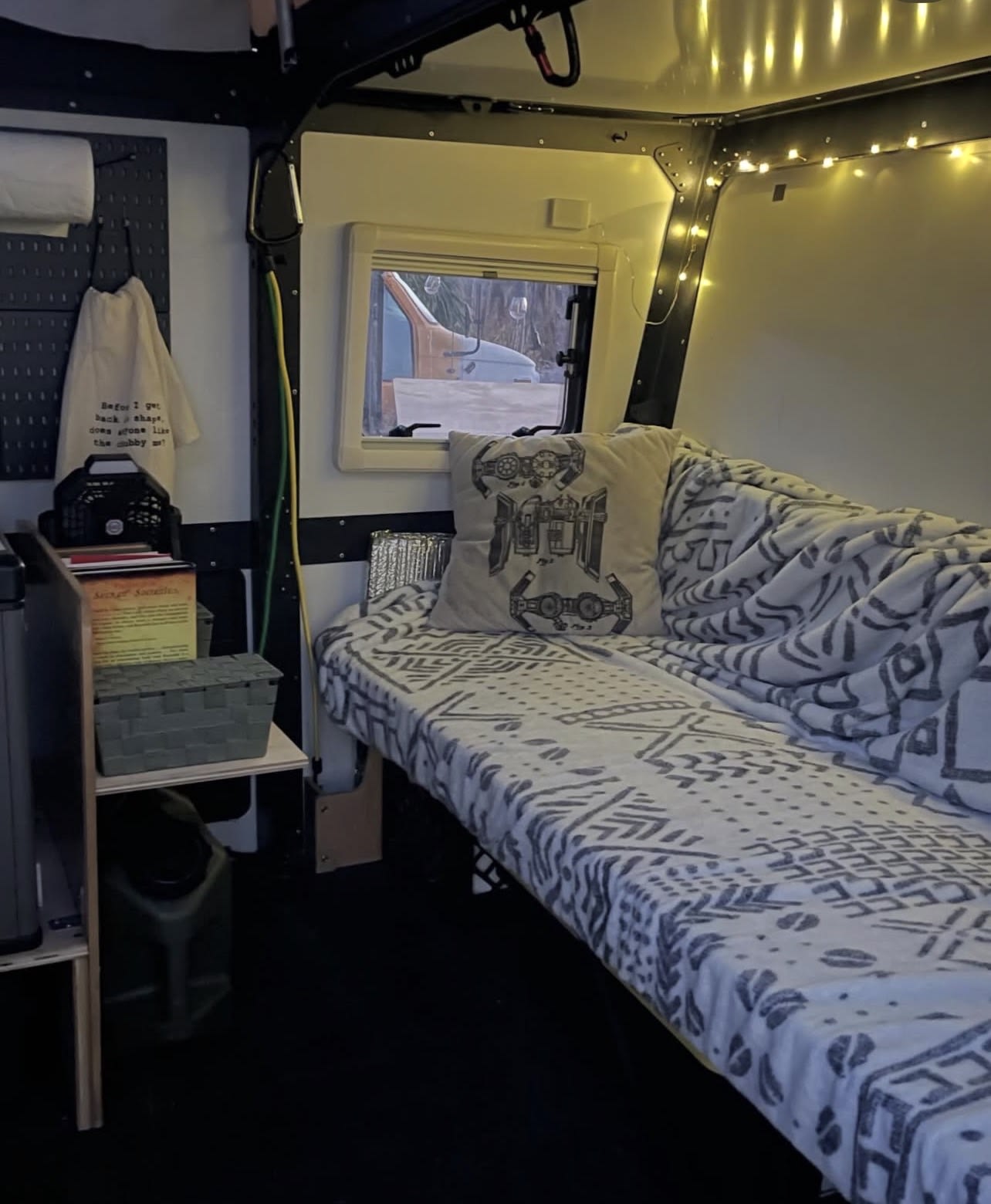 Cozy interior of an RV rental featuring a bed with patterned blanket, Star Wars pillow, ambient string lights, and a window view.. TAXA TAXA Trailer 2020