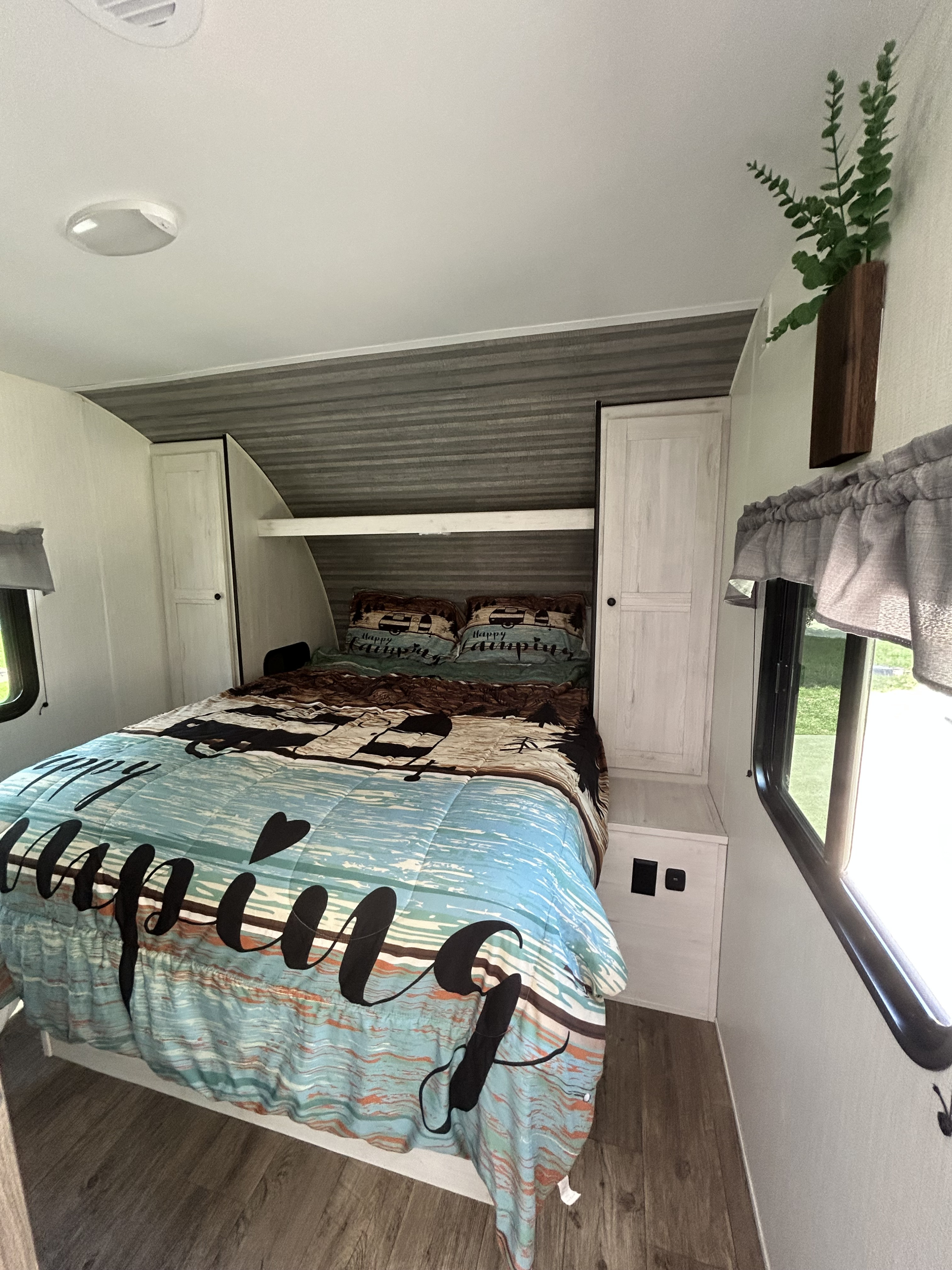 Cozy RV rental bedroom features a "Happy Camping" themed bed, built-in storage, and window for natural light.. Heartland RVs Trail Runner 2024