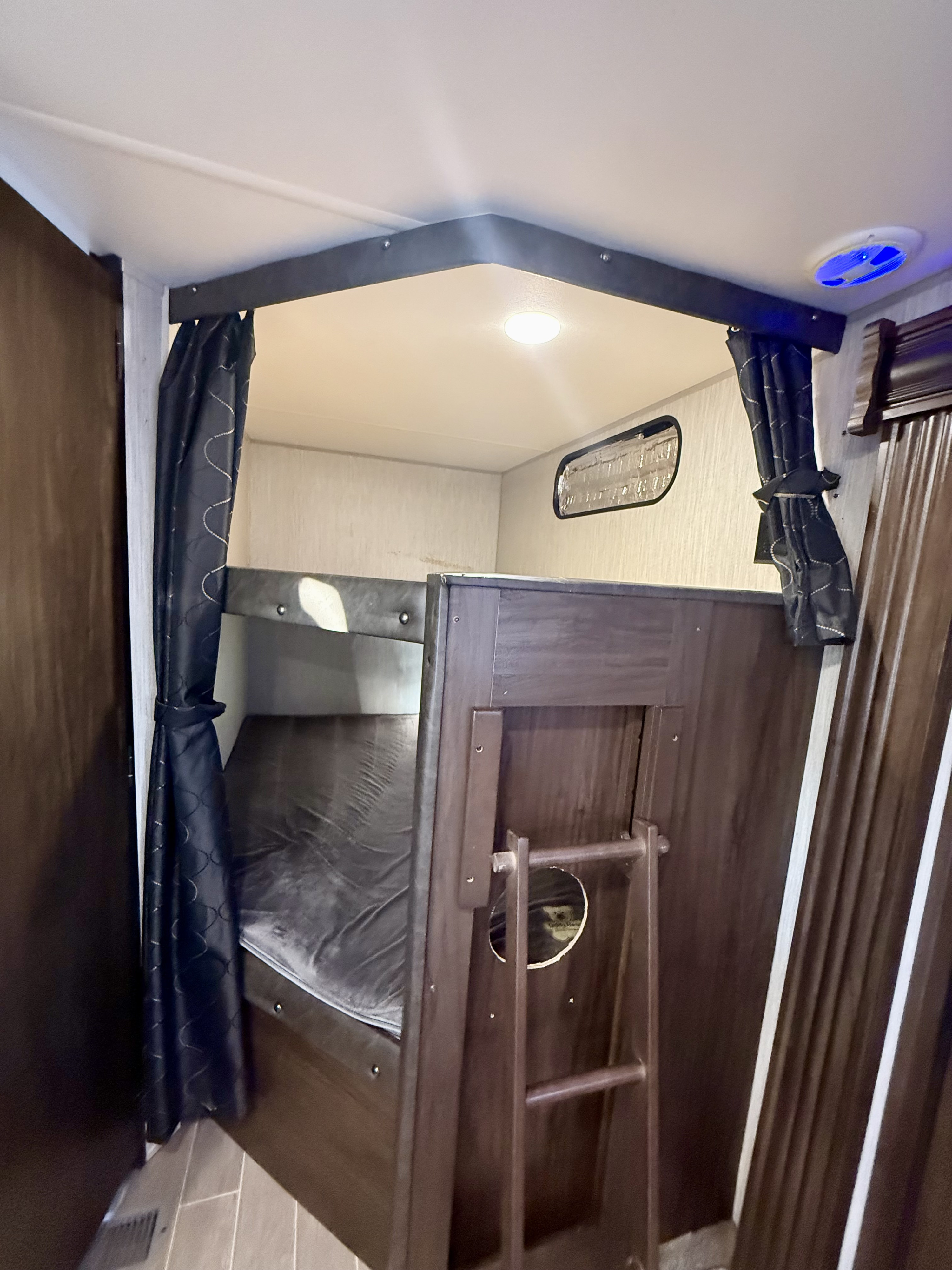 Cozy bunk bed area in an RV rental, featuring privacy curtains, a ladder, and overhead lighting.. Forest River Cherokee 2021