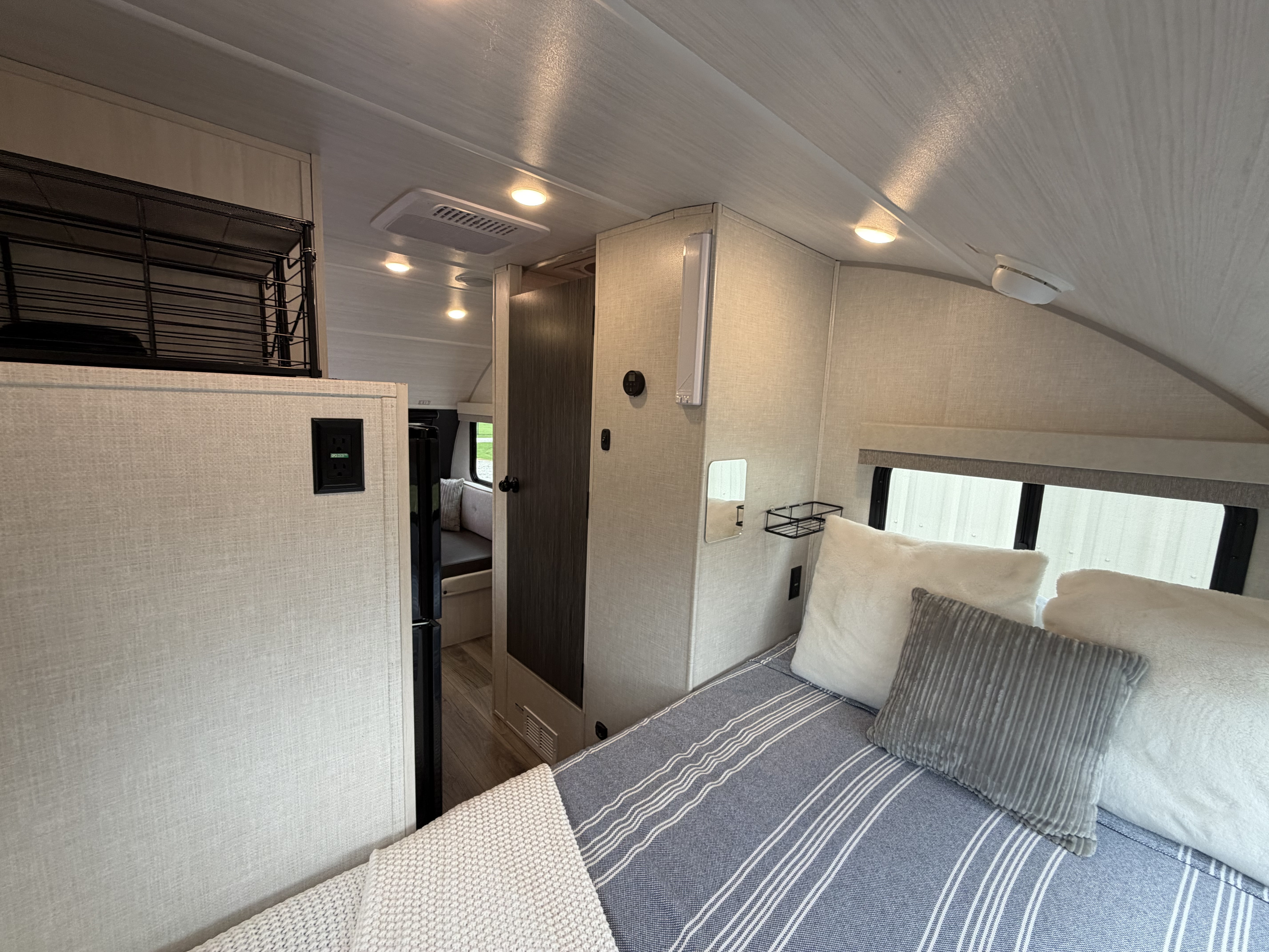 Cozy rv rental bedroom showing blue striped bedding, textured walls, overhead lighting, and compact storage.. R-Pod R-Pod Trailer 2025