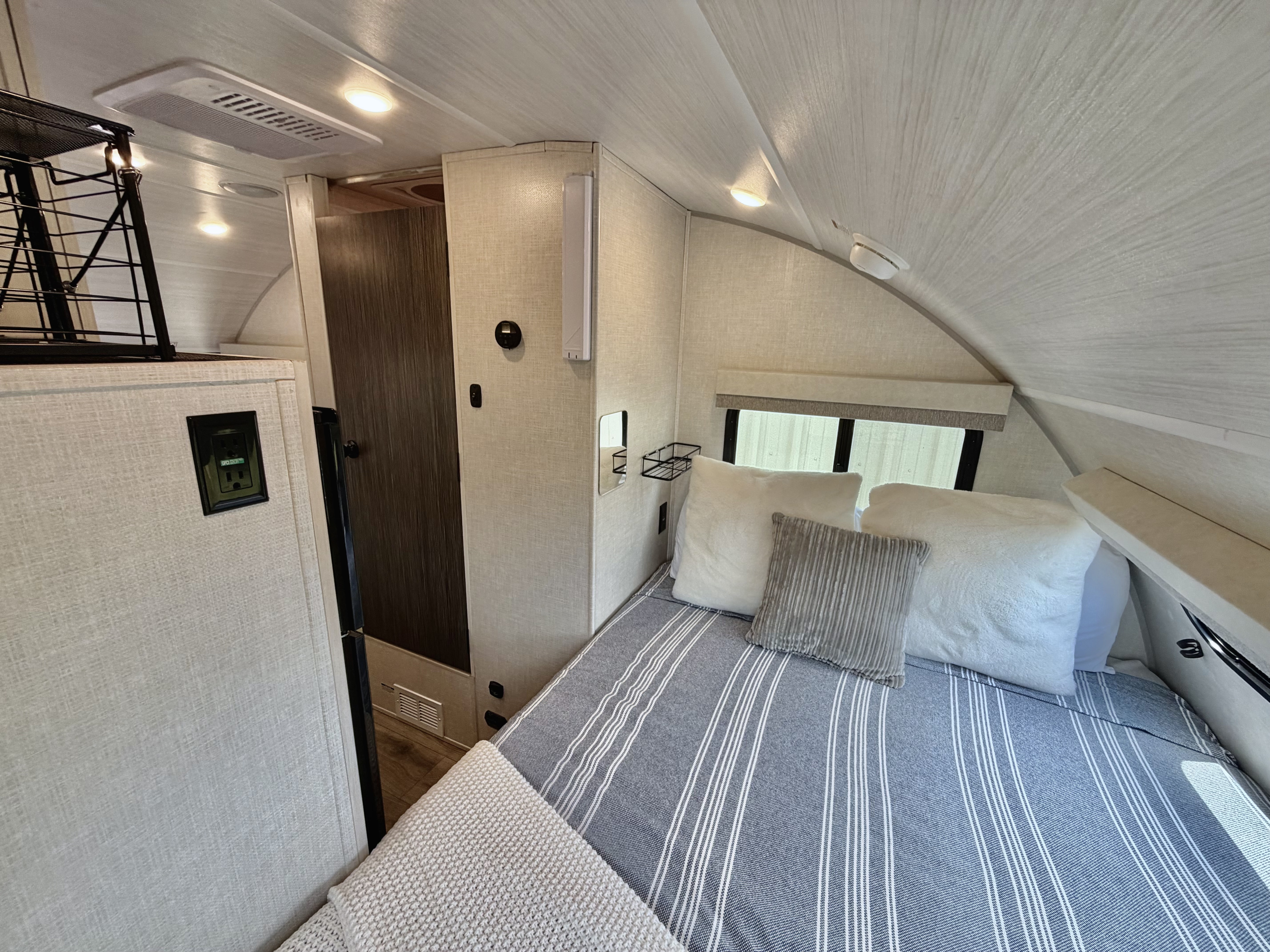 Cozy RV rental bedroom with a striped bed, plush pillows, textured walls, overhead lighting, and compact amenities.. R-Pod R-Pod Trailer 2025