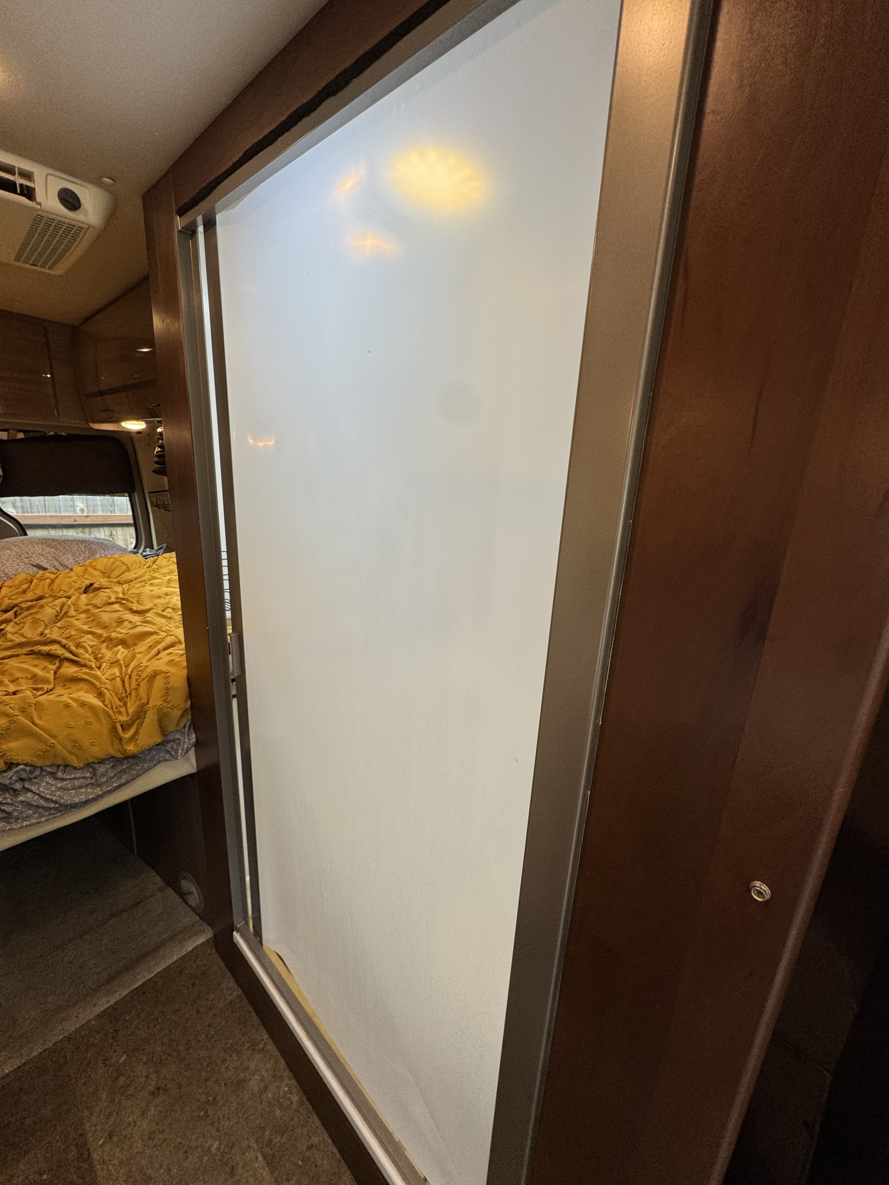 RV rental interior: a frosted sliding door next to dark wood cabinetry, revealing a bedroom with a bed and overhead AC unit.. ERA ERA Class B 2015
