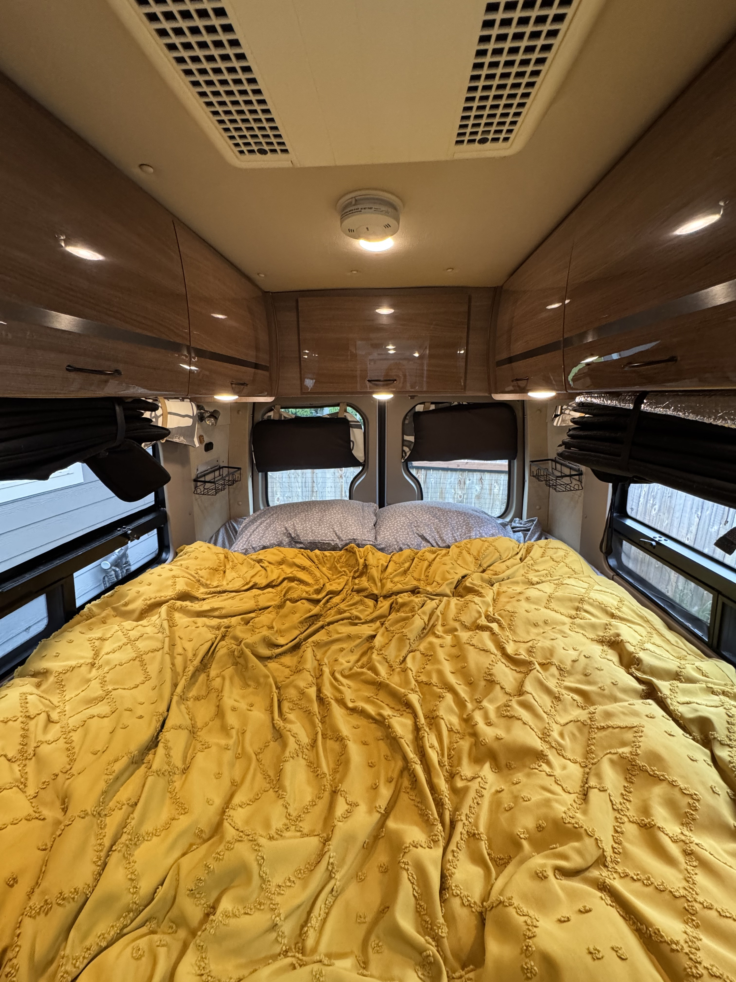 Cozy rv rental bedroom interior featuring a comfortable yellow bed, overhead storage, and windows, perfect for travel.. ERA ERA Class B 2015