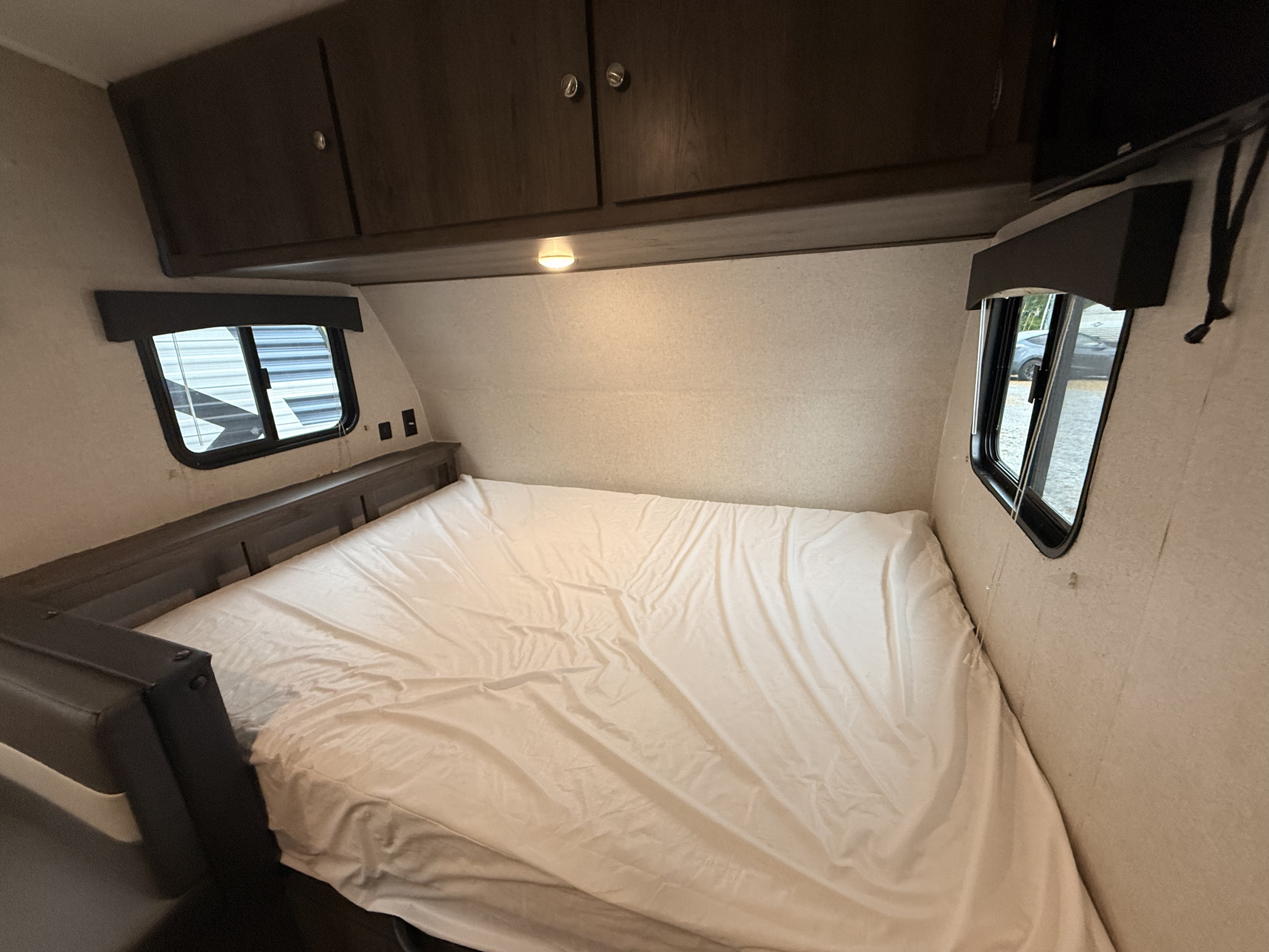 Clean RV rental bedroom featuring a comfortable bed with a white sheet, overhead cabinets, and two windows.. Forest River Viking Saga 2021