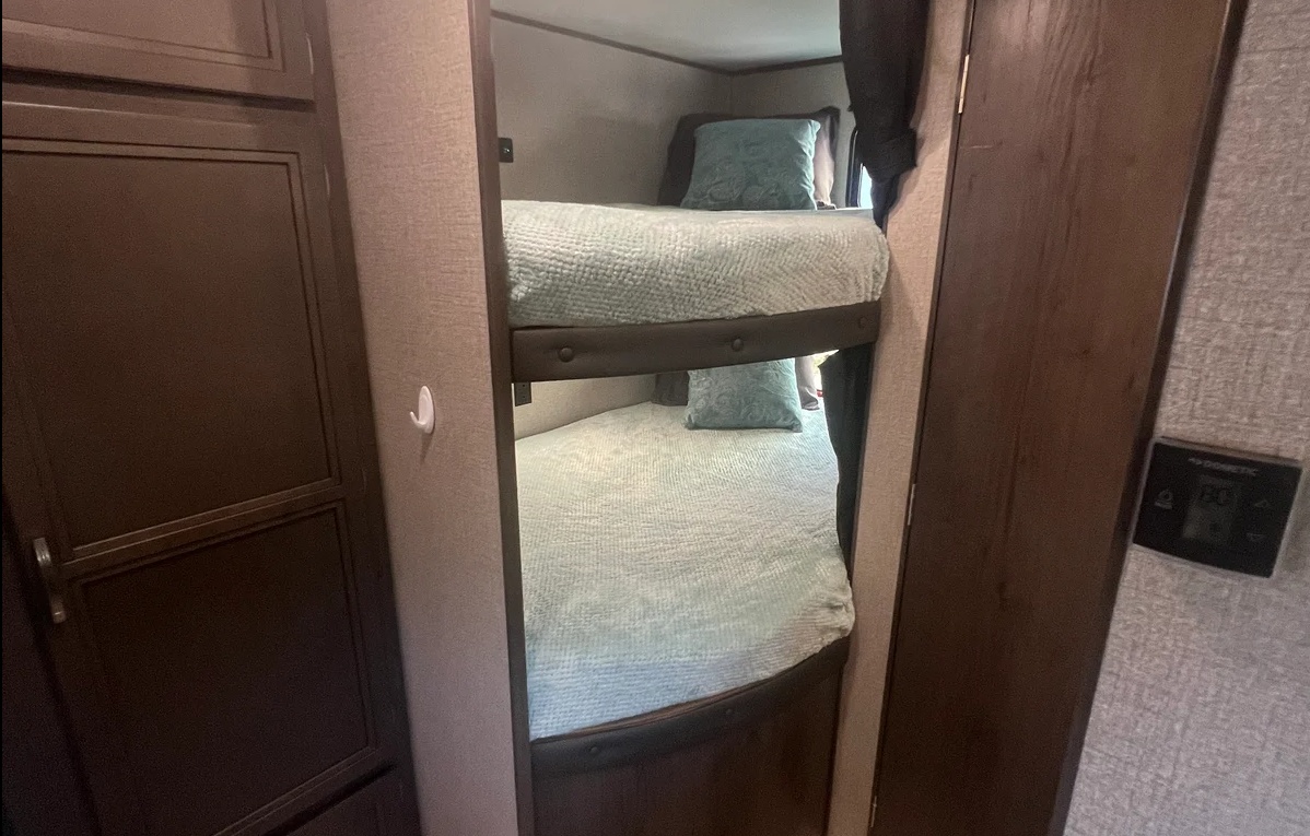 RV rental features cozy bunk beds with light blue bedding. A closet is on the left, a Dometic thermostat on the right wall.. Jayco Jay Flight SLX 2021